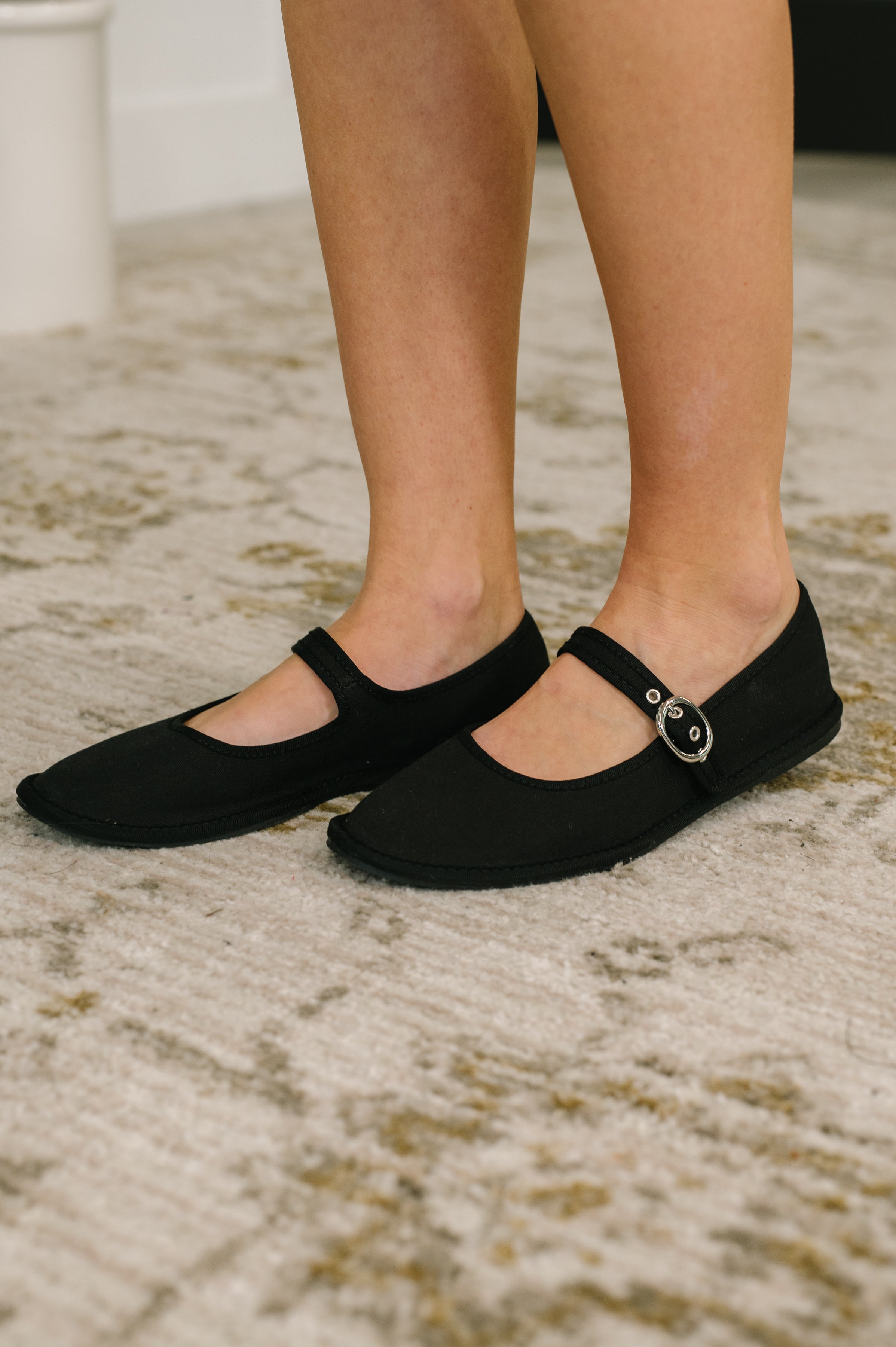 Black buckle strap flats worn on feet indoors over a patterned rug