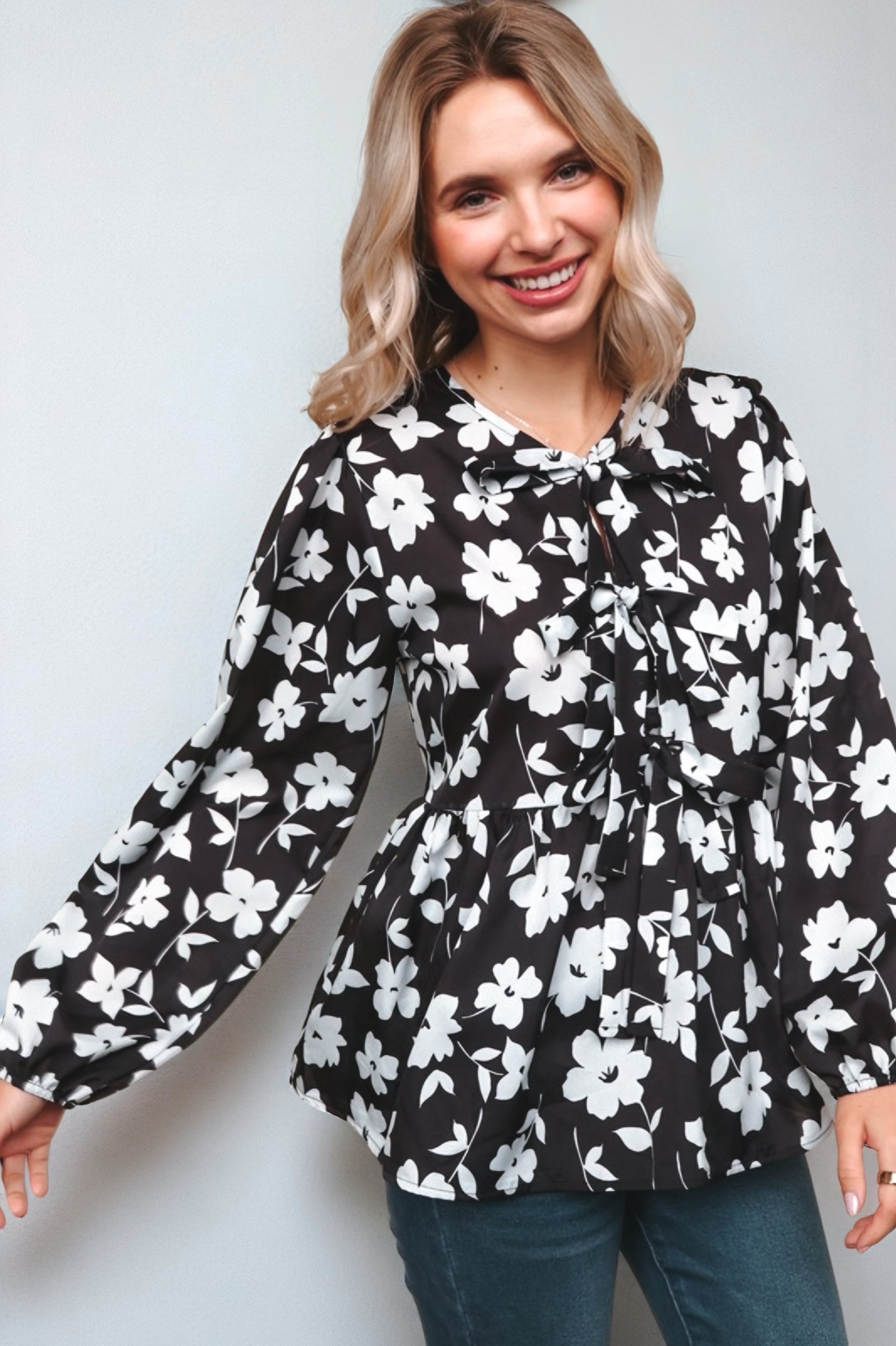 Fleur with Flair Double Bow Babydoll Top in black and white floral print with long sleeves and front bow detail, worn by a smiling woman with wavy blonde hair.