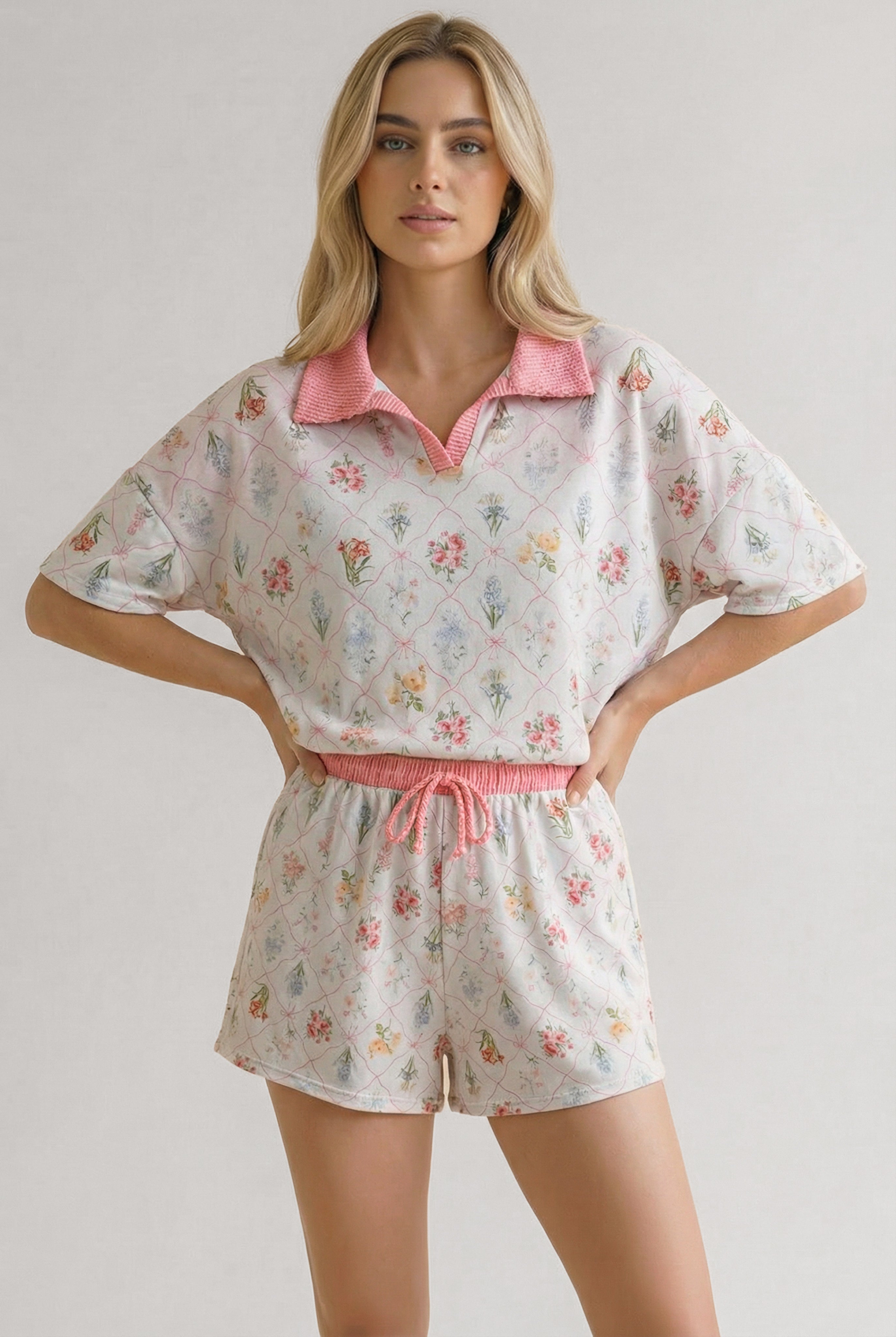 Woman wearing ivory floral print matching short set with pink collar and waistband, standing with hands on hips
