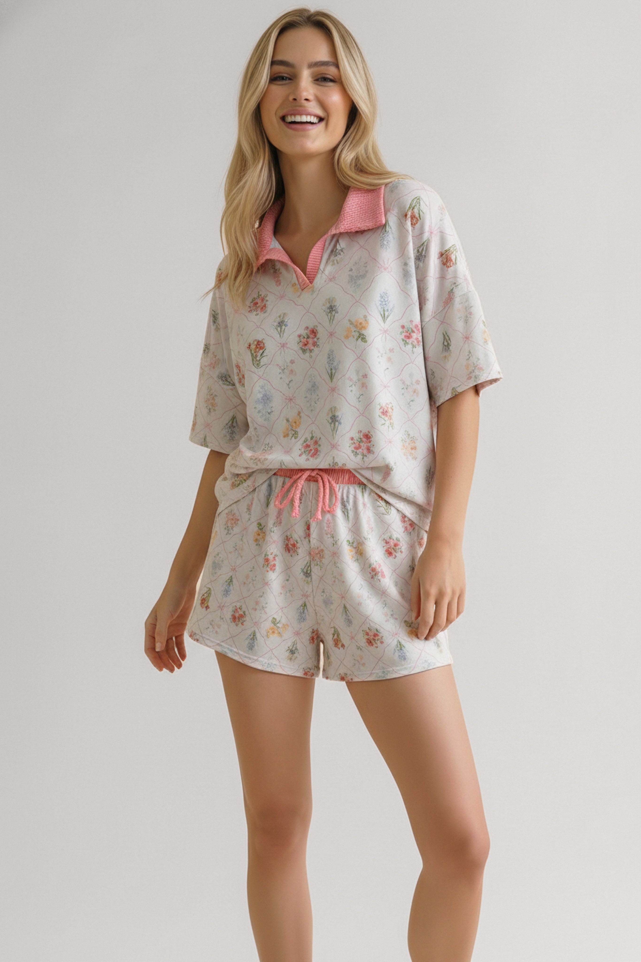 Woman smiling wearing ivory floral print short set with pink collar and drawstring, posing with hand in pocket