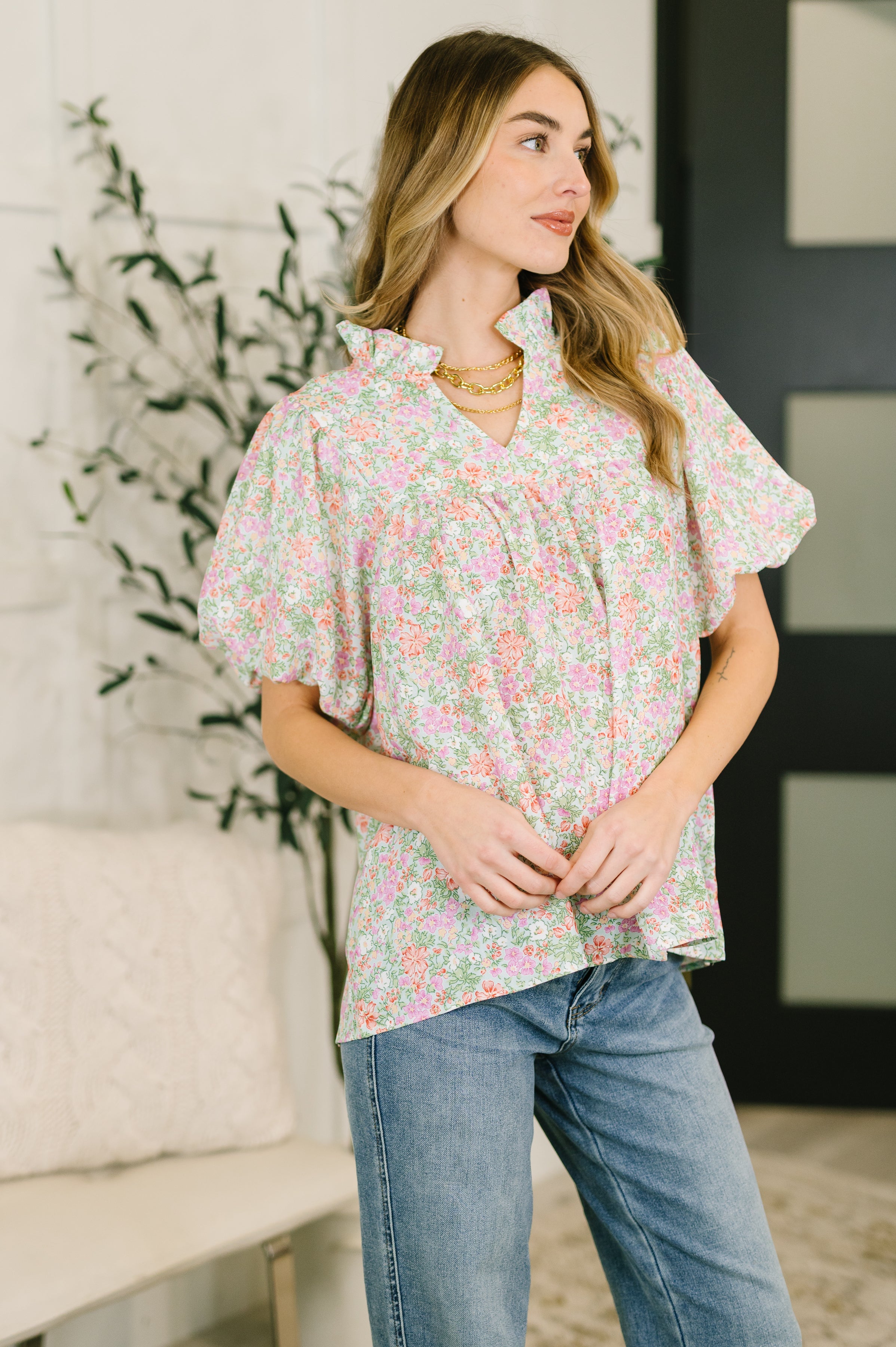 Woman wearing pastel floral blouse with ruffled notch neckline and balloon sleeves paired with denim jeans indoors