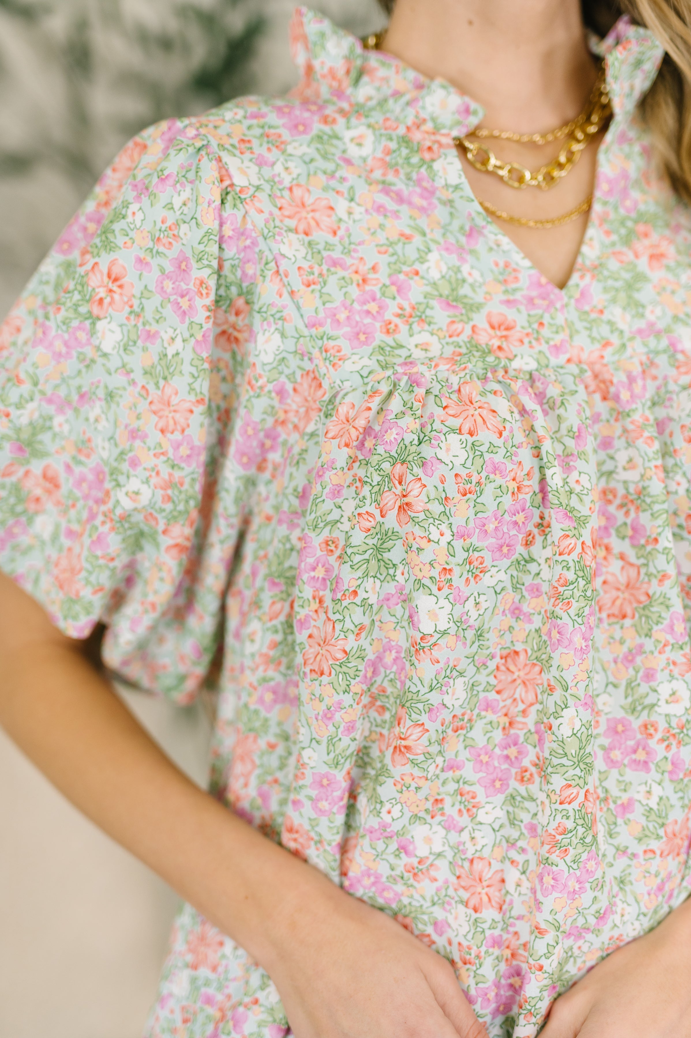 Close-up of blouse with pastel floral print, ruffled notch neckline, and voluminous puff sleeves in lightweight fabric
