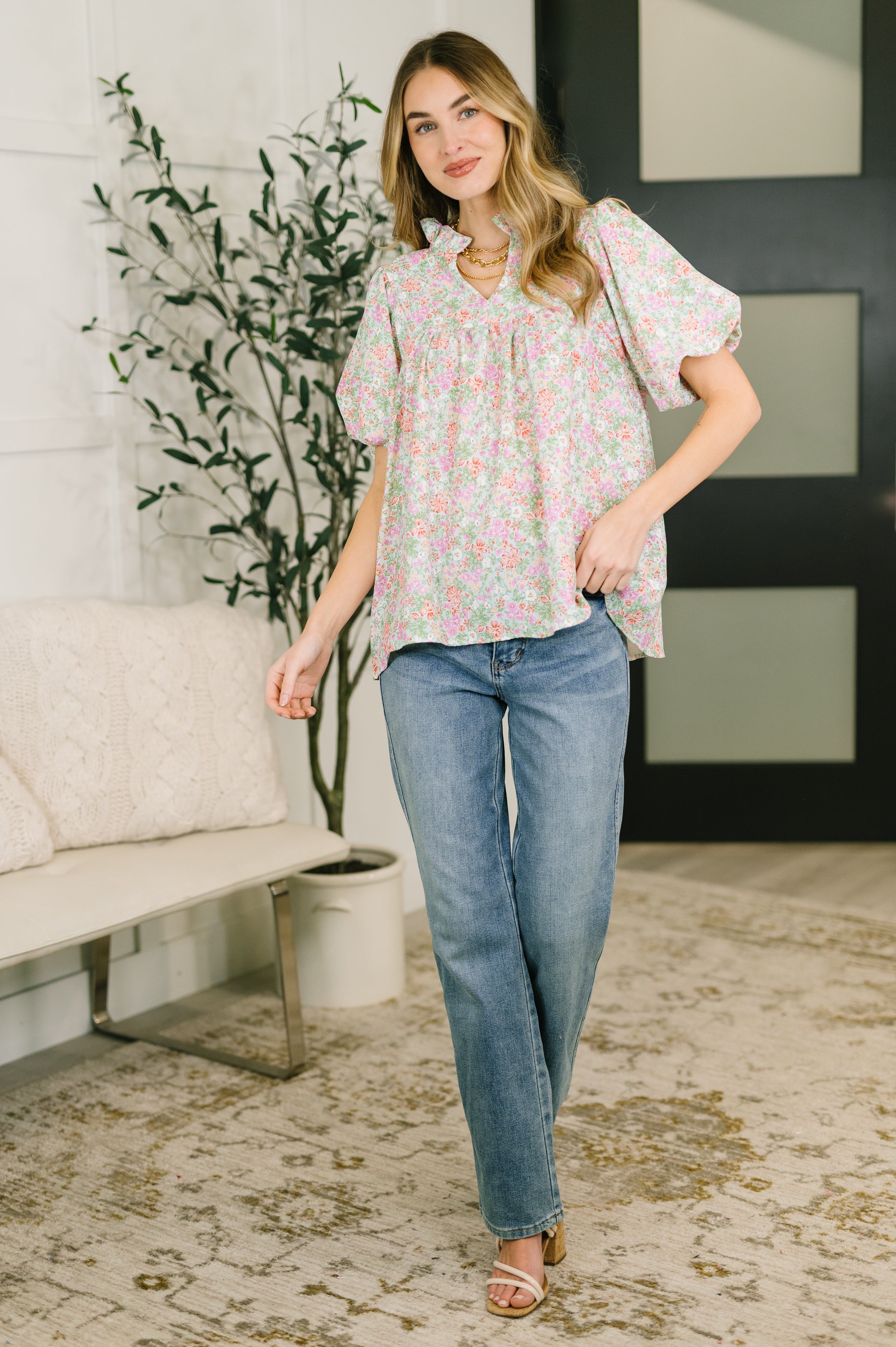 Woman wearing pastel floral notch neck blouse with puff sleeves paired with straight-leg blue jeans indoors