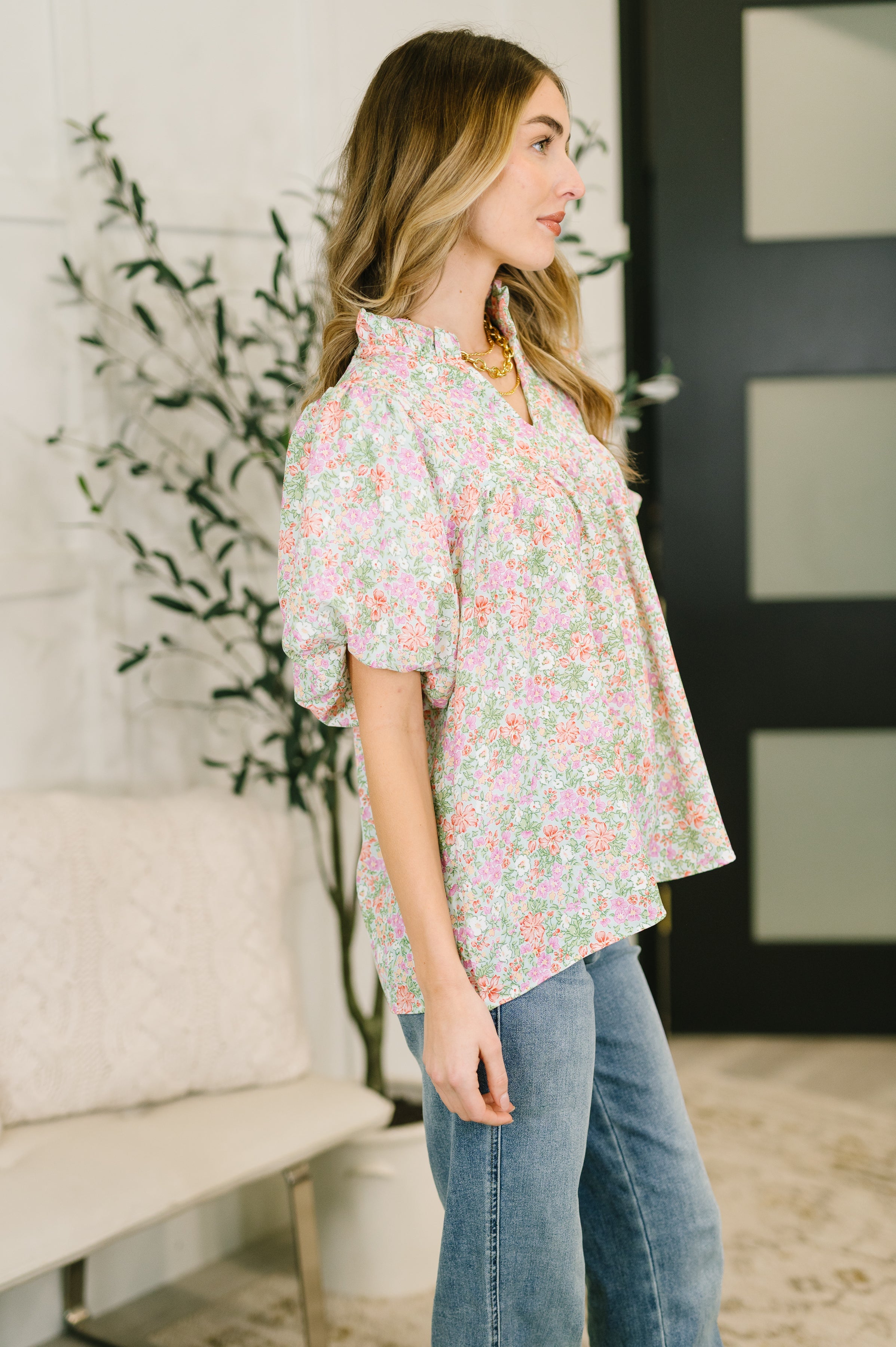 Side view of woman wearing floral notch neck blouse with puff sleeves and relaxed fit paired with blue jeans indoors