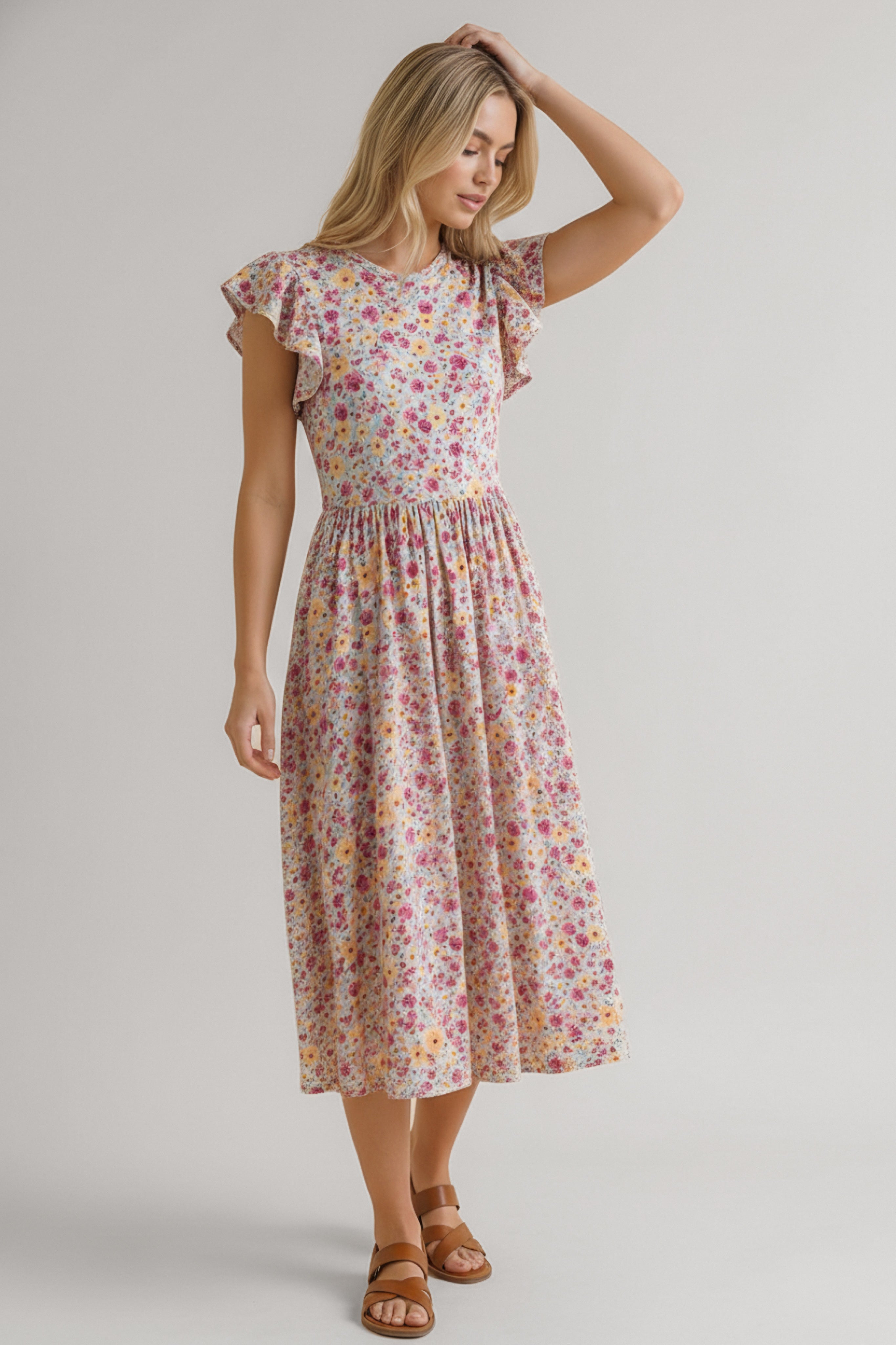 Woman in a pink floral midi dress with flutter sleeves and a gathered waist paired with brown flat sandals