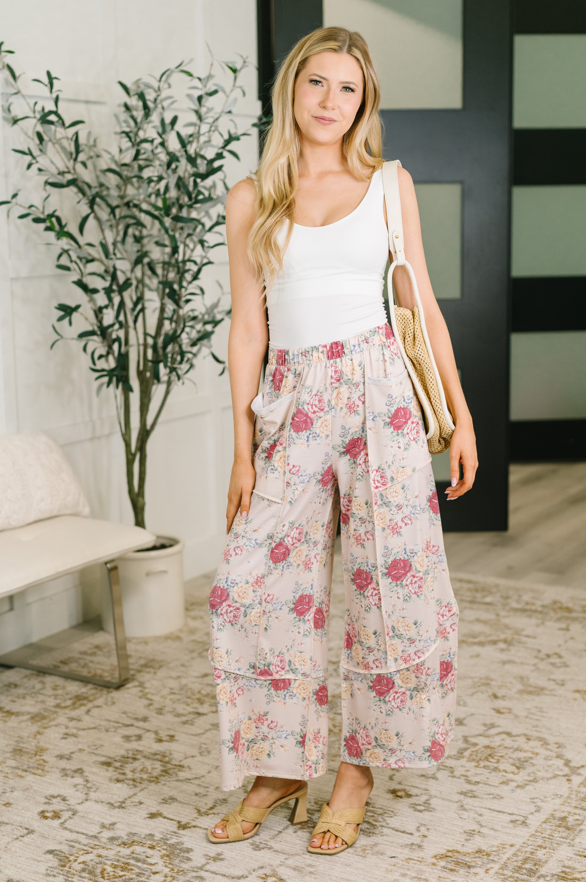 Woman wearing pink floral wide leg bottoms with a white tank top indoors