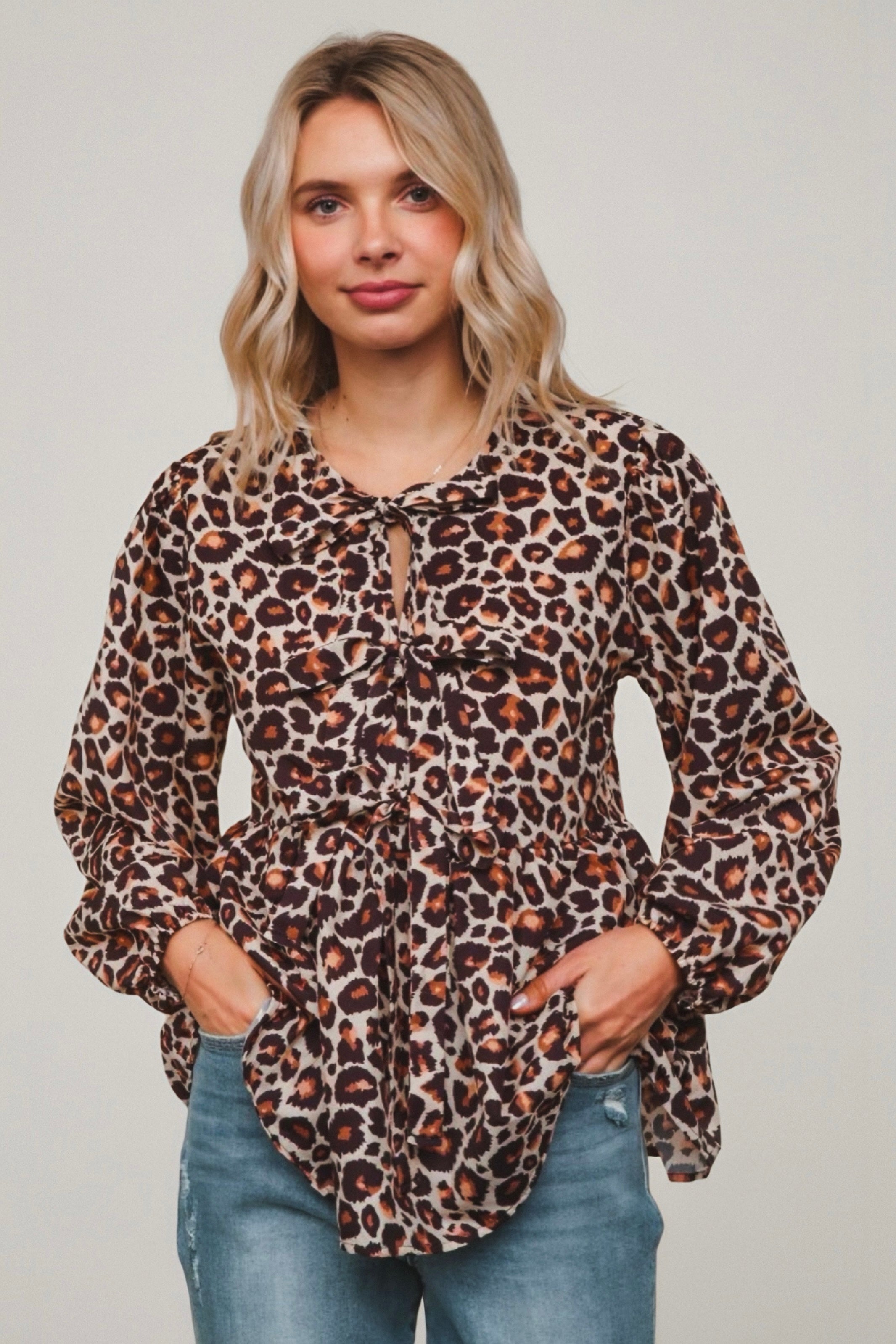 Woman wearing brown spotted babydoll blouse with tie front and gathered waist paired with light blue jeans
