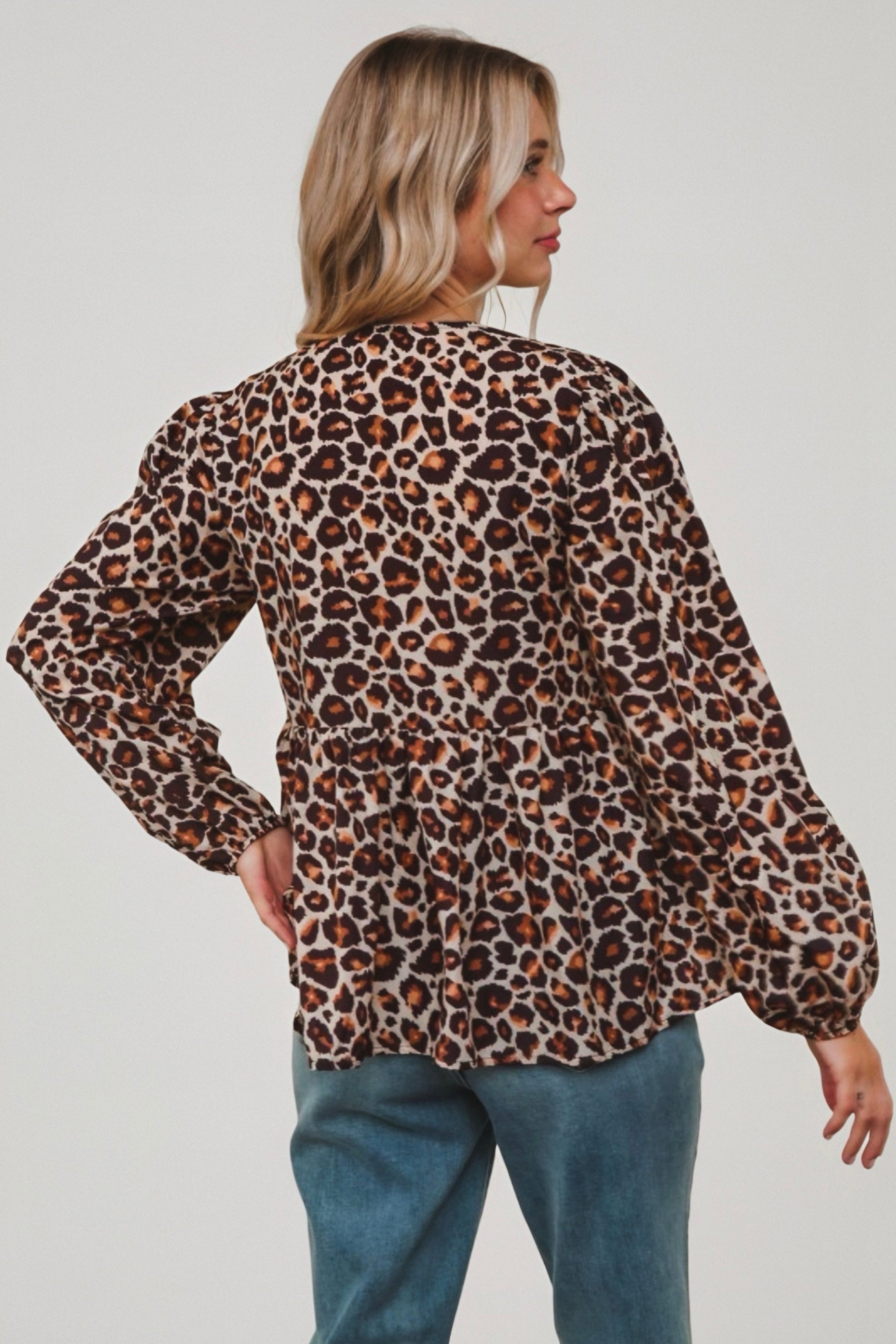 Woman seen from behind wearing brown leopard print babydoll blouse with gathered peplum hem and long sleeves paired with blue jeans