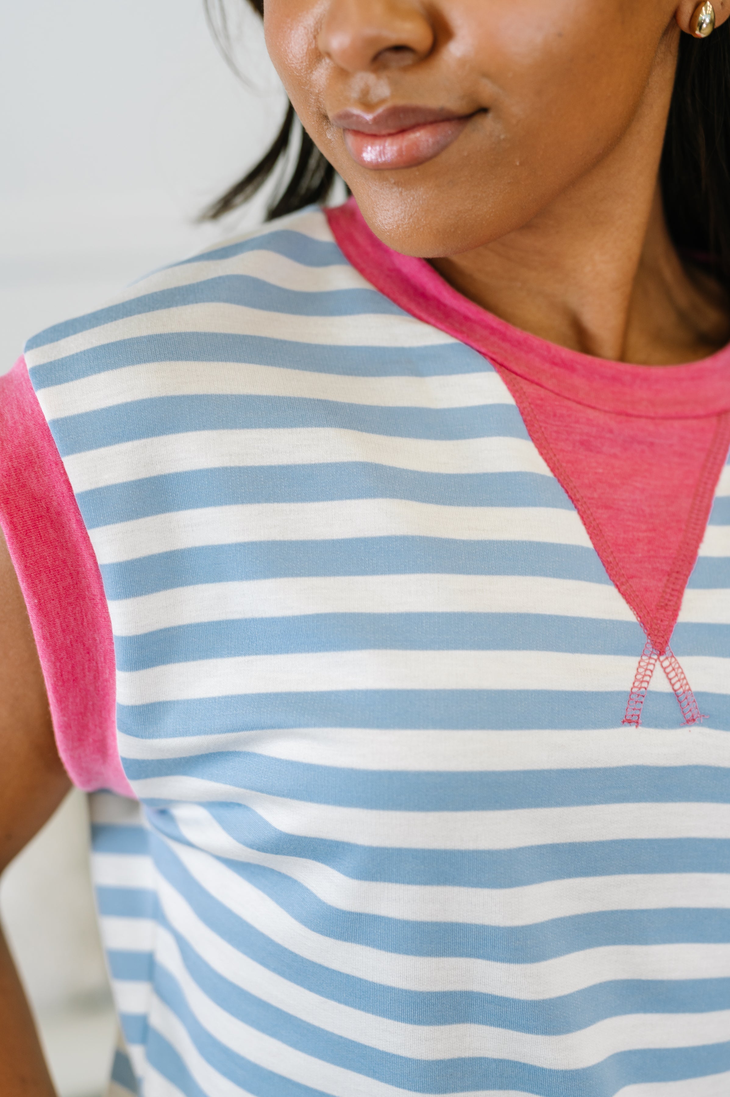 Close-up of person wearing a blue and white striped muscle tee with vibrant pink trim in an eclectic, free-spirited style