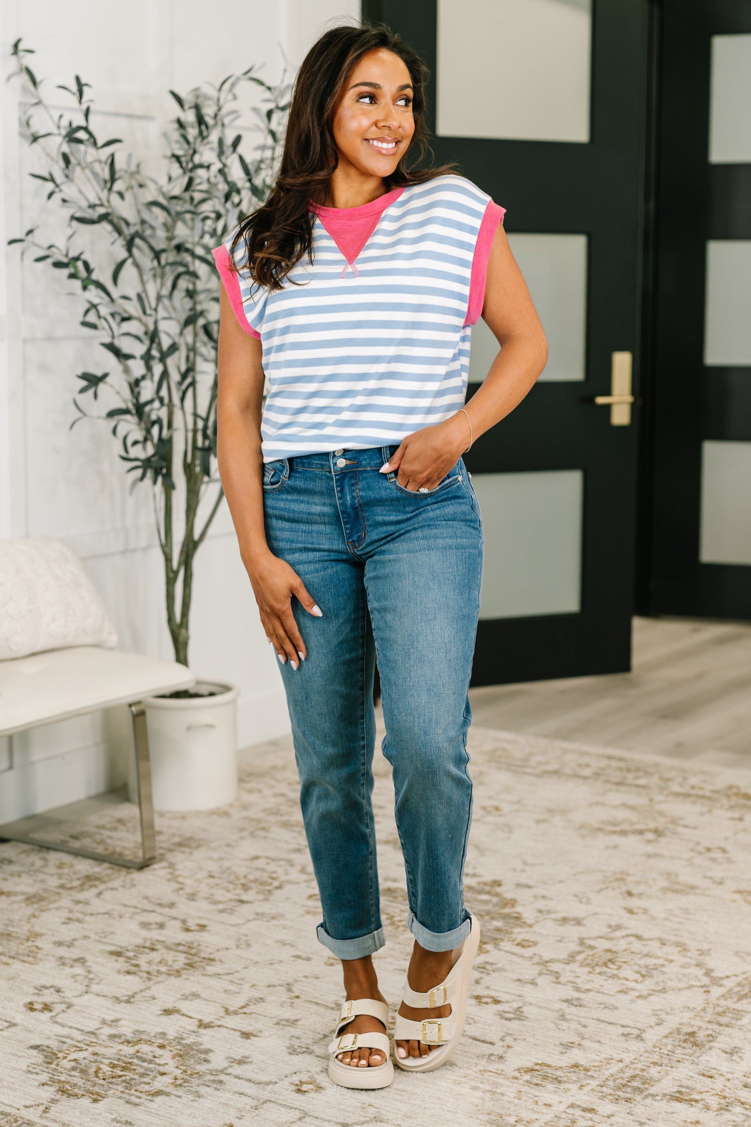 Woman wearing a relaxed color block muscle tee with blue stripes and pink accents paired with rolled cuff jeans in eclectic setting