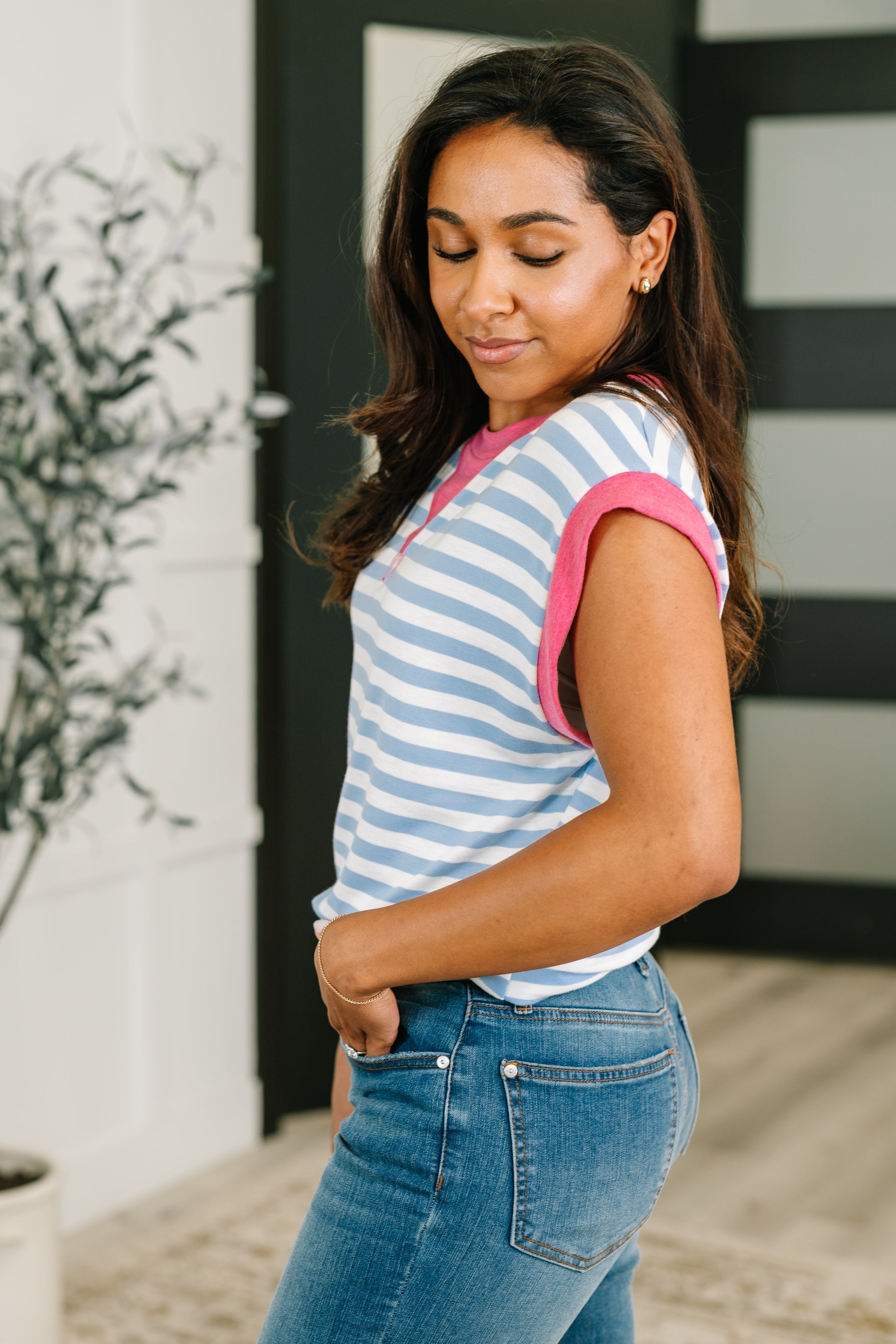 Woman wearing a blue and white striped muscle tee with pink trim, paired with blue jeans in an eclectic indoor space
