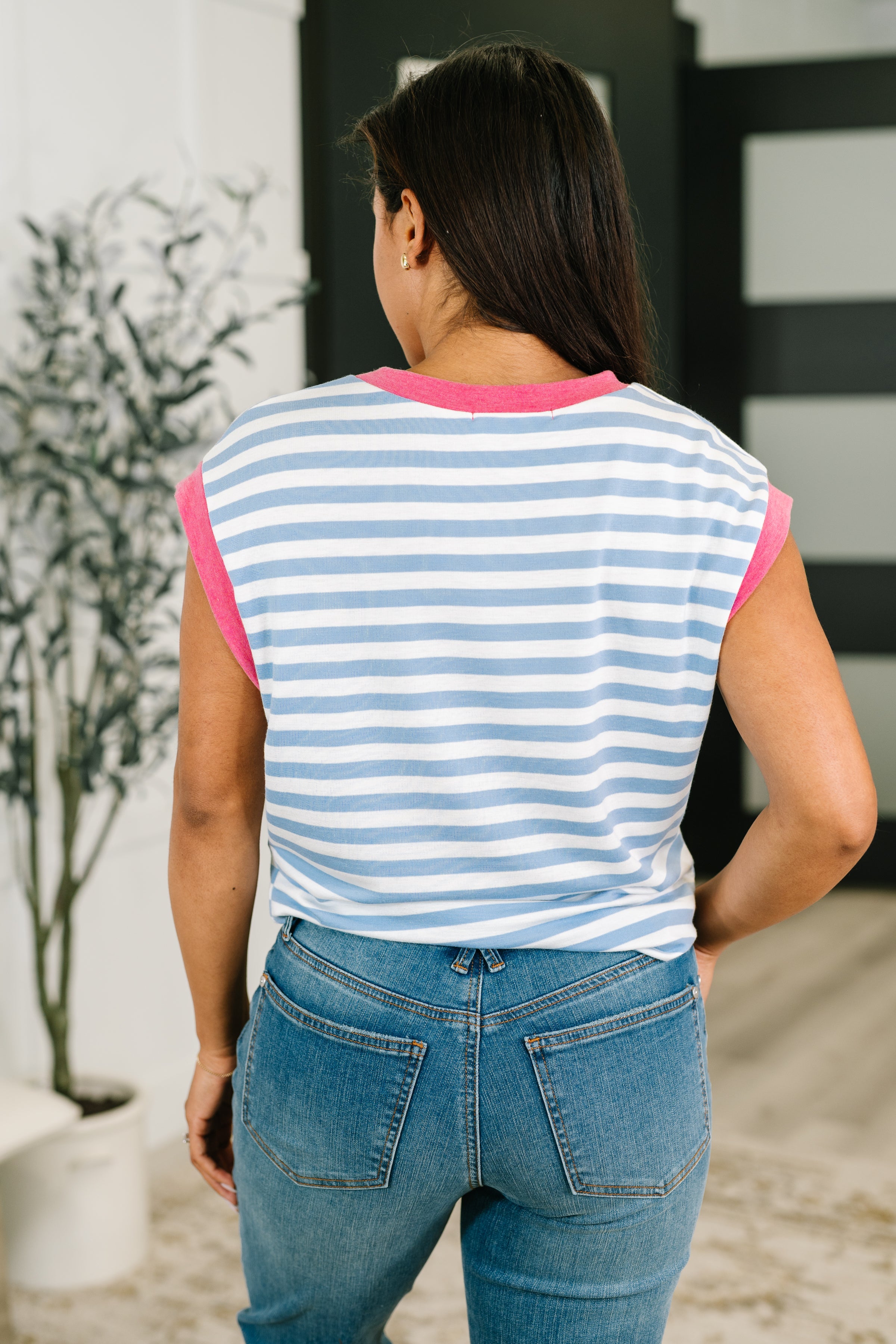 Woman wearing a blue and white striped muscle tee with pink trim, paired with casual denim jeans in a bright eclectic room