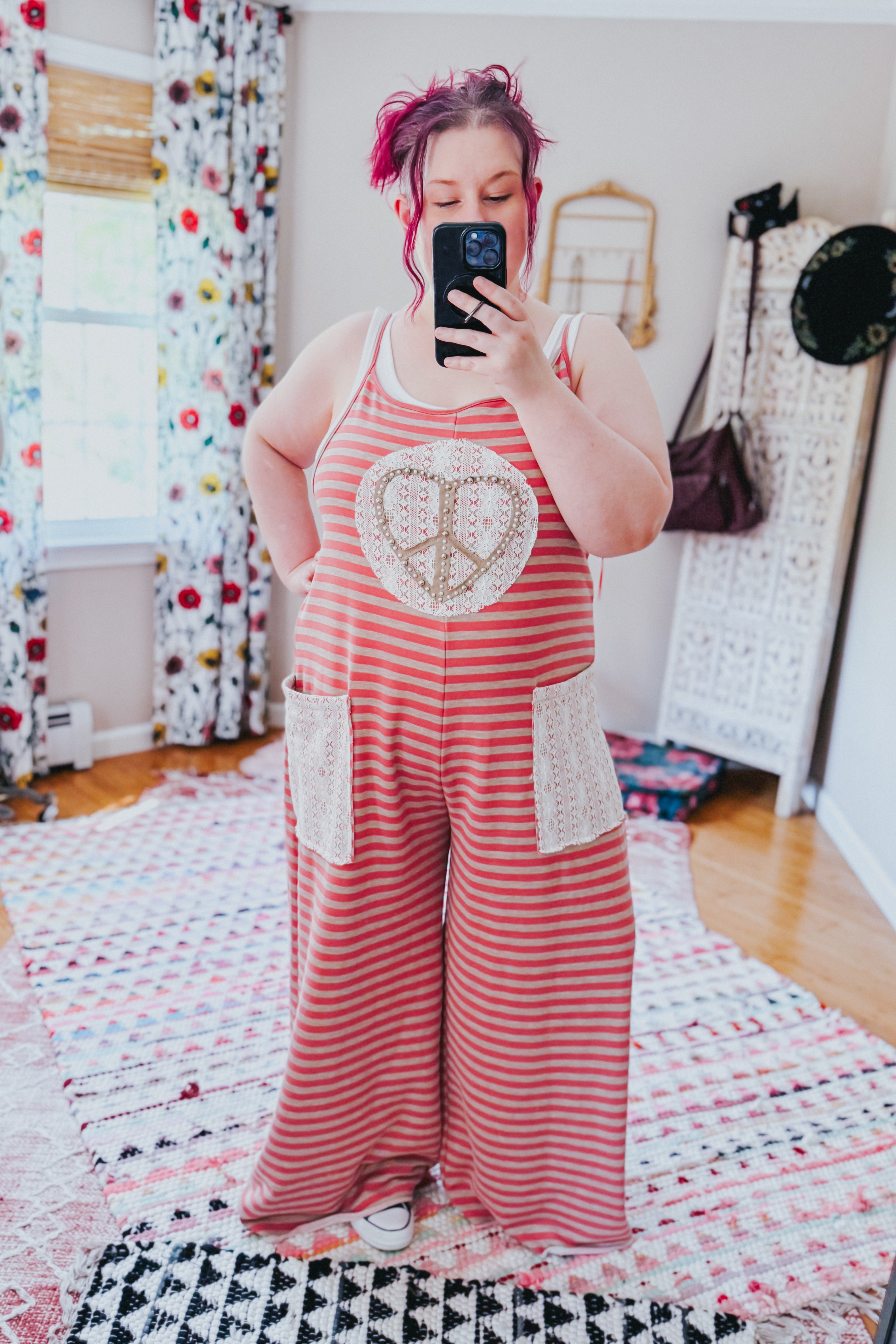 Plus size woman wearing relaxed red and beige striped sleeveless jumpsuit with lace patch pockets and peace sign applique taking selfie