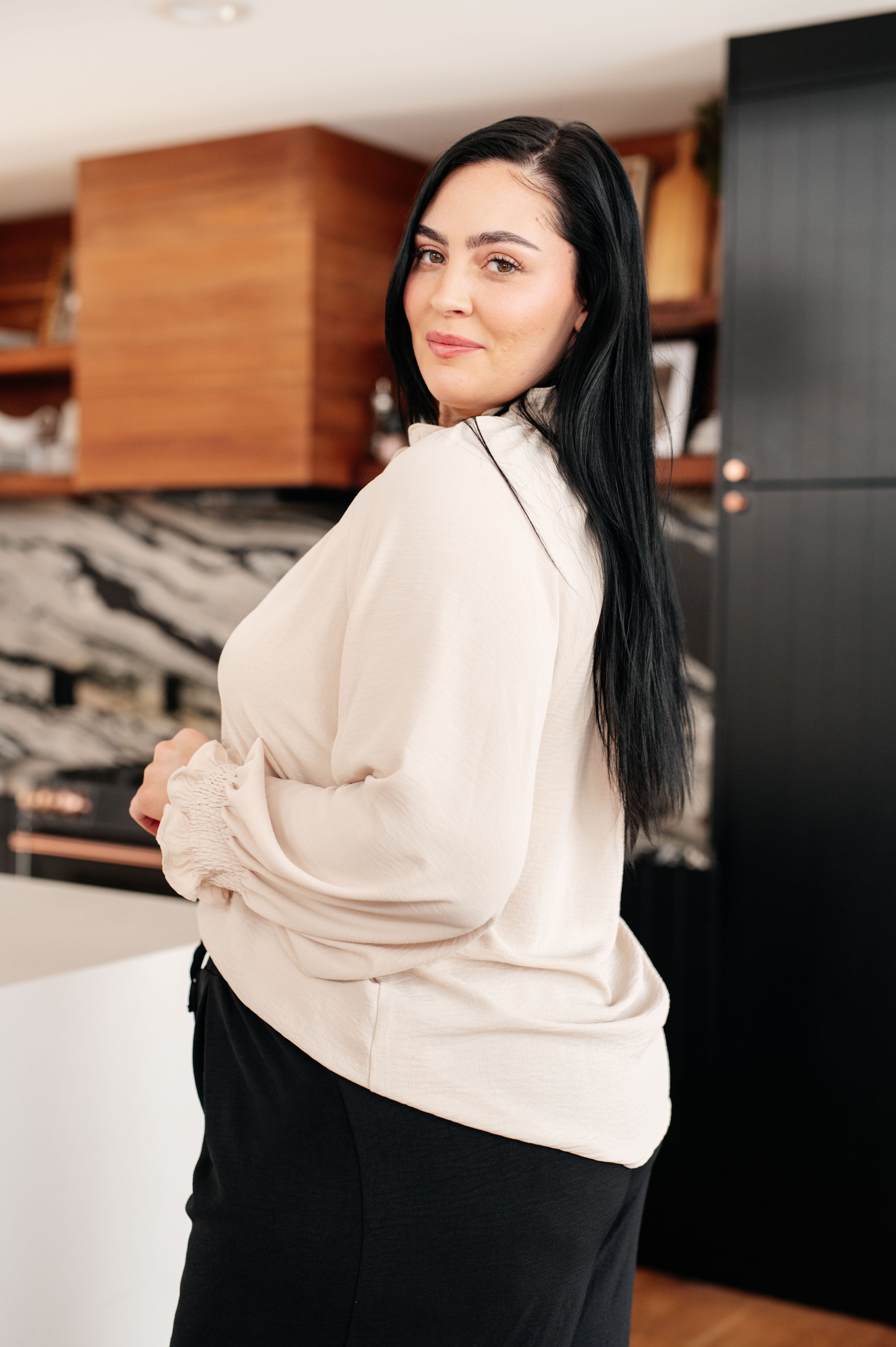 Side view of cream button-up blouse with subtle puff sleeves and smocked elastic cuffs worn by model indoors