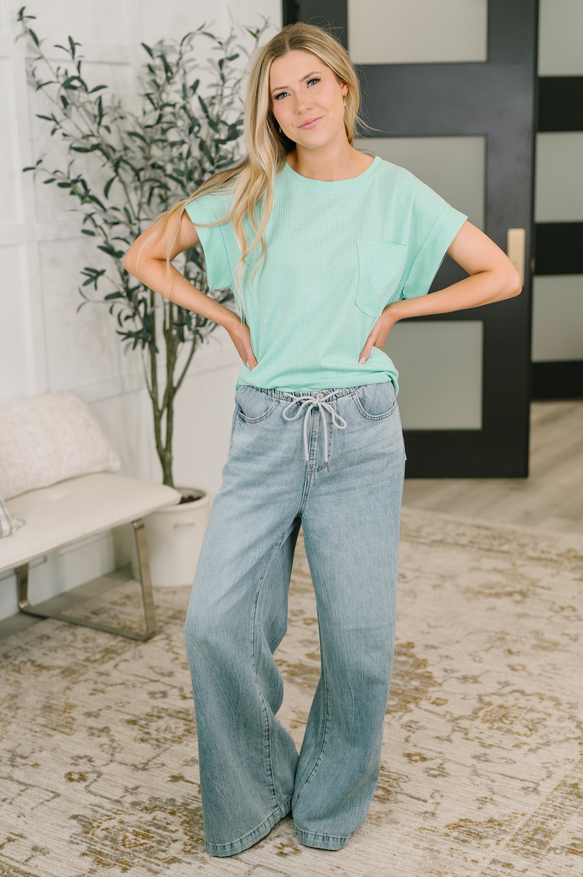 Woman wearing a relaxed mint waffle knit tee styled with loose light denim jeans in an eclectic, free-spirited setting
