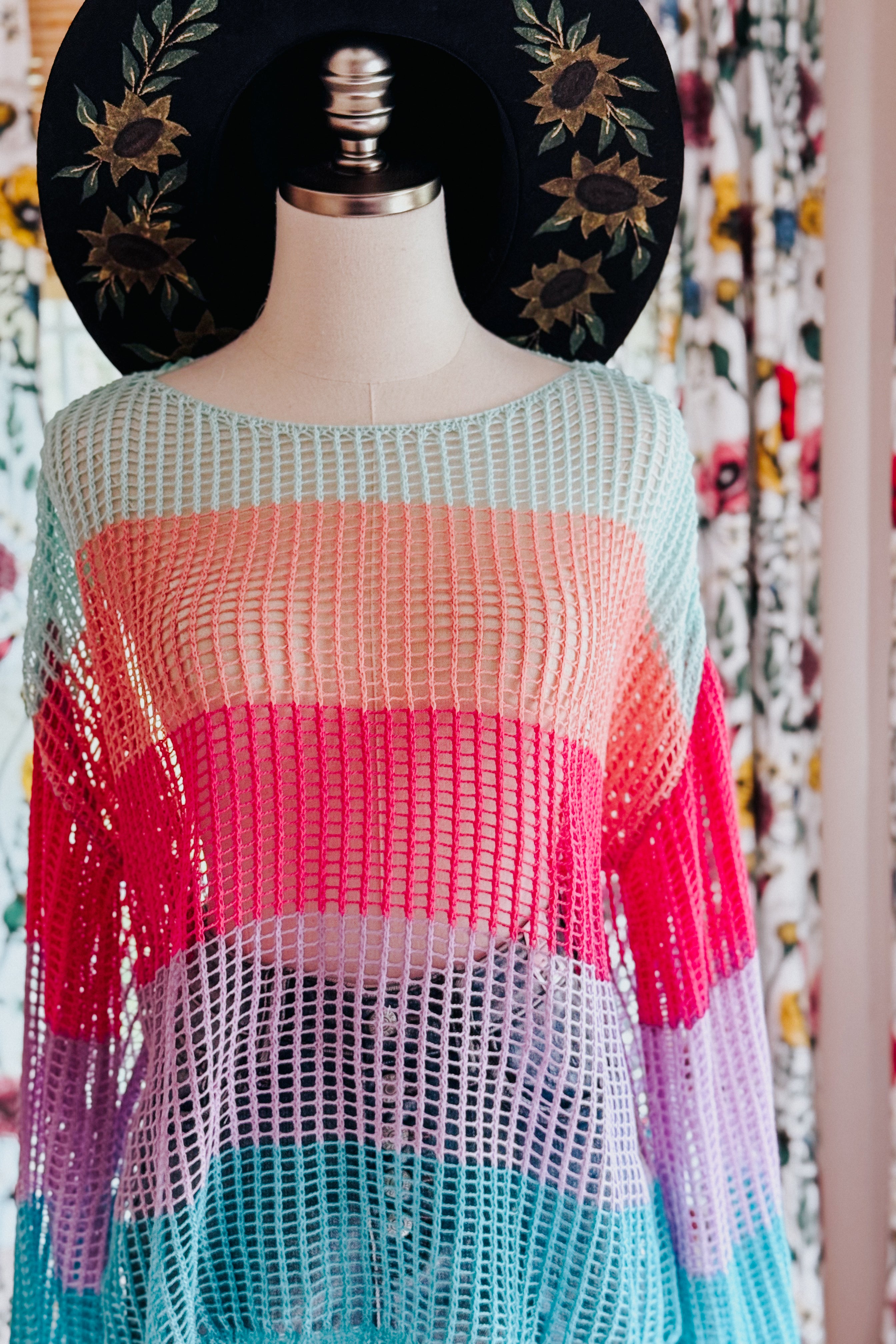 Multicolor striped crochet mesh pullover with wide bell sleeves on mannequin wearing black sunflower embroidered hat