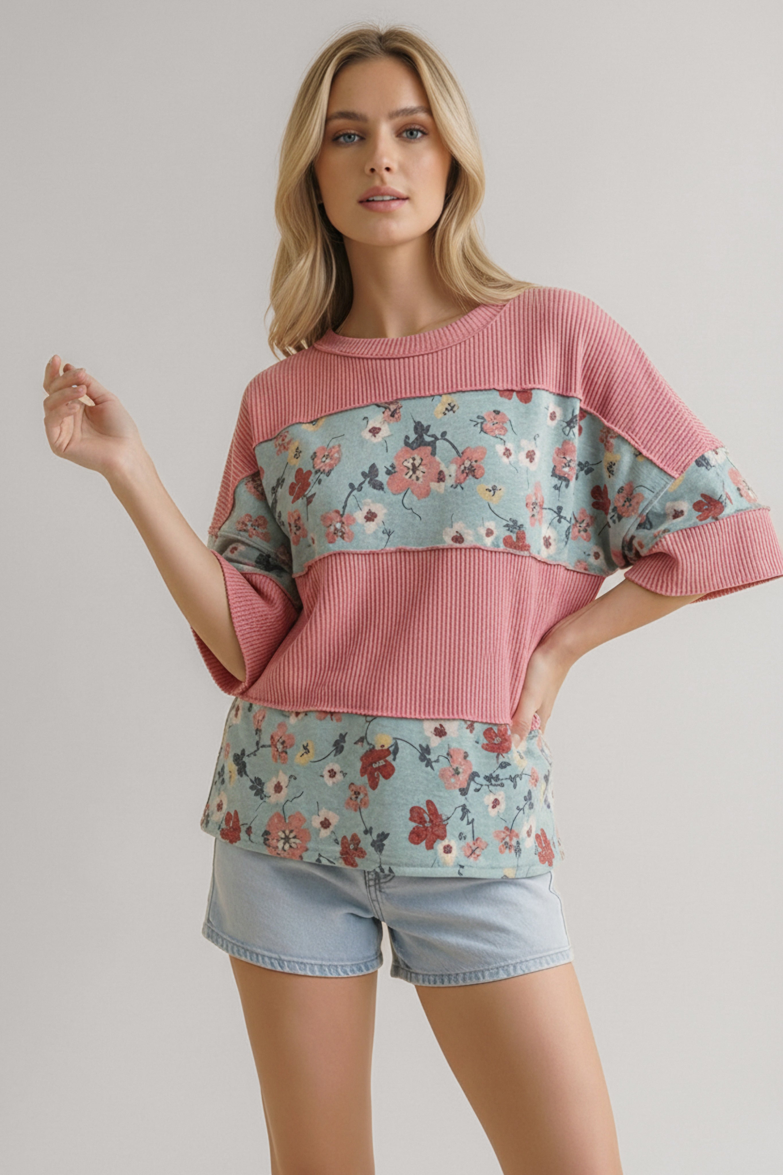 Woman wearing a pink floral colorblock top with ribbed knit panels paired with light blue denim shorts against a neutral backdrop