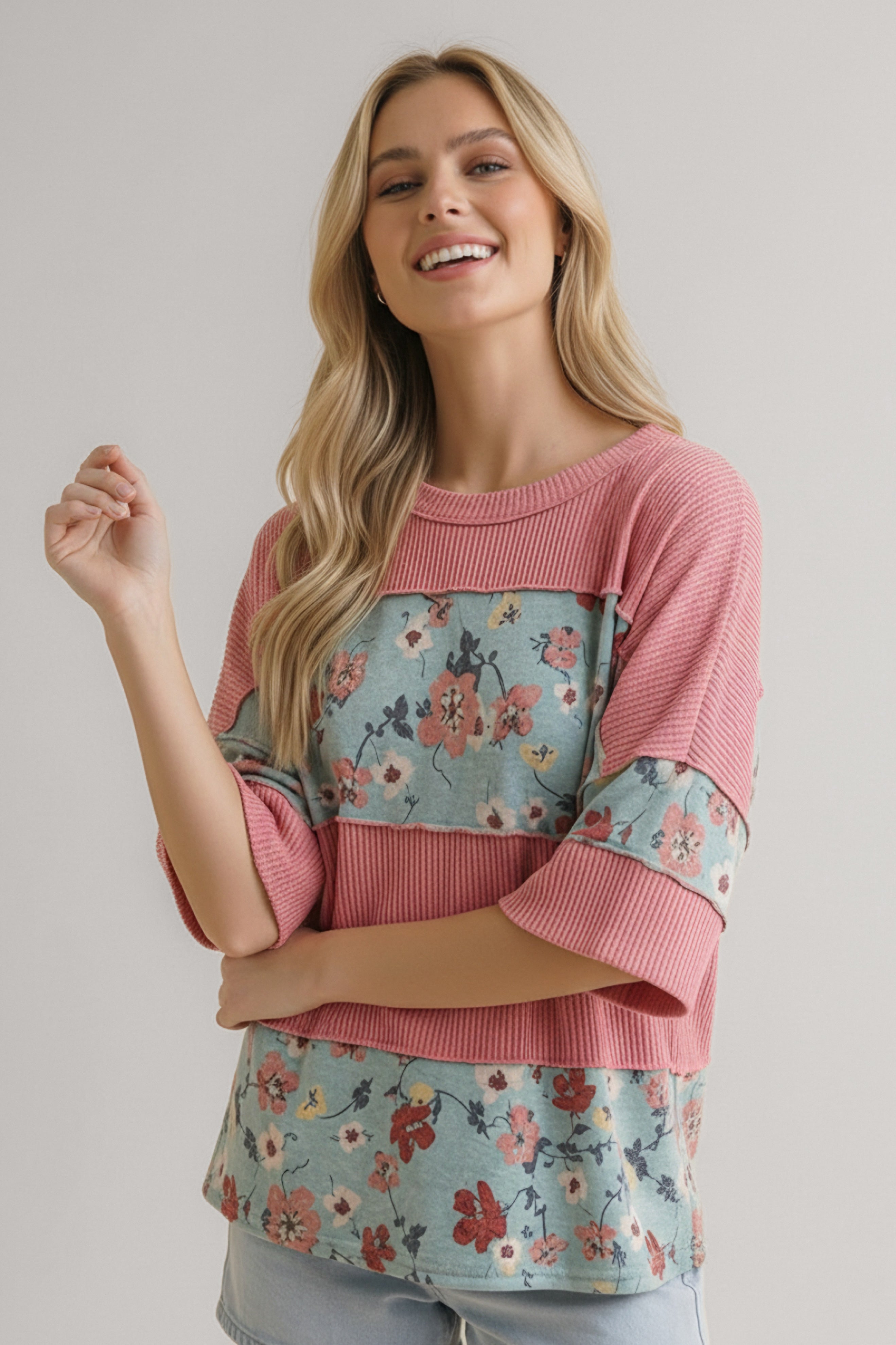 Woman wearing pink ribbed colorblock top with blue floral panels and three-quarter sleeves smiling indoors