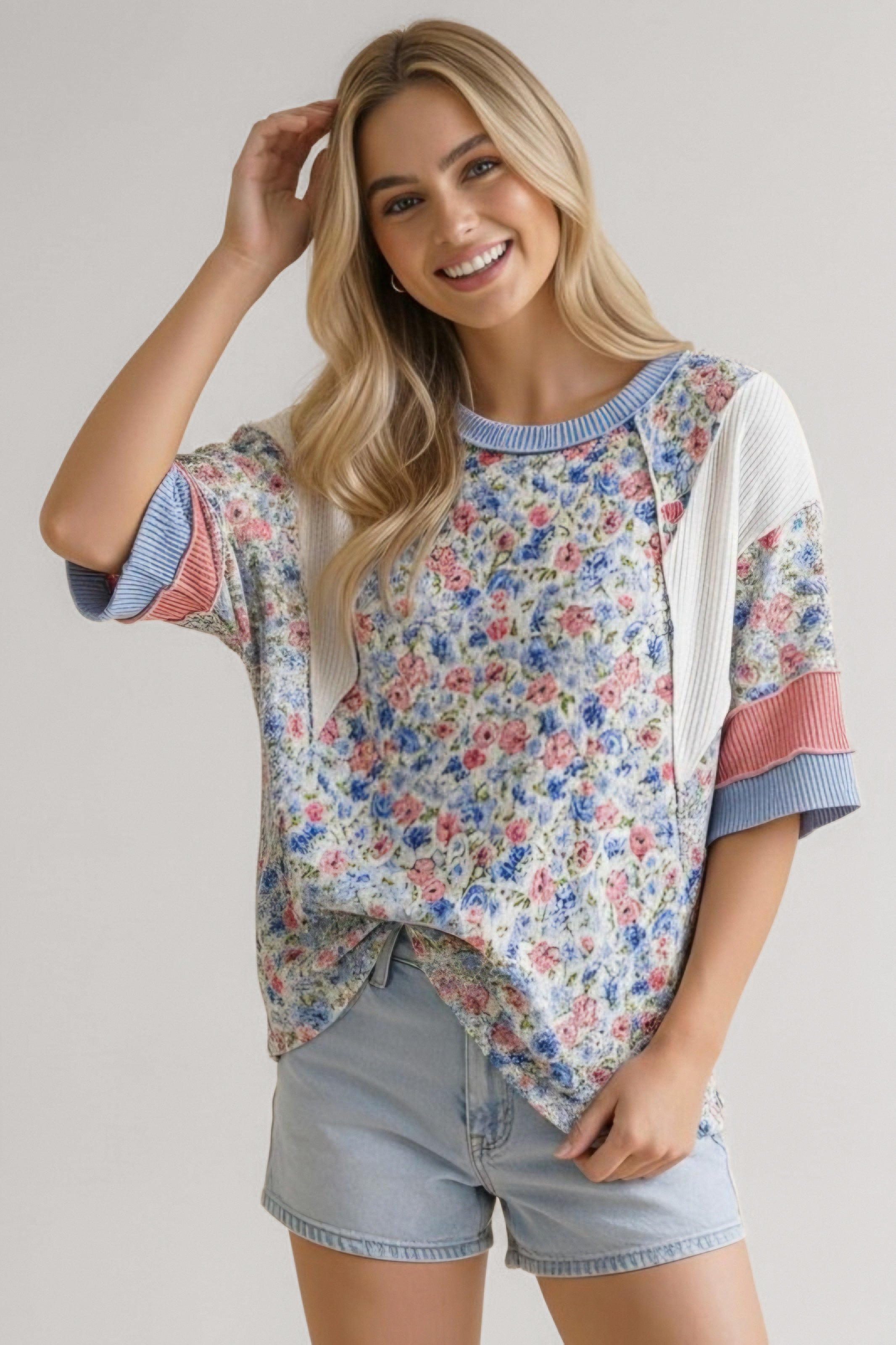 Smiling woman wearing blue floral mixed media top with ribbed colorblock sleeves and light denim shorts