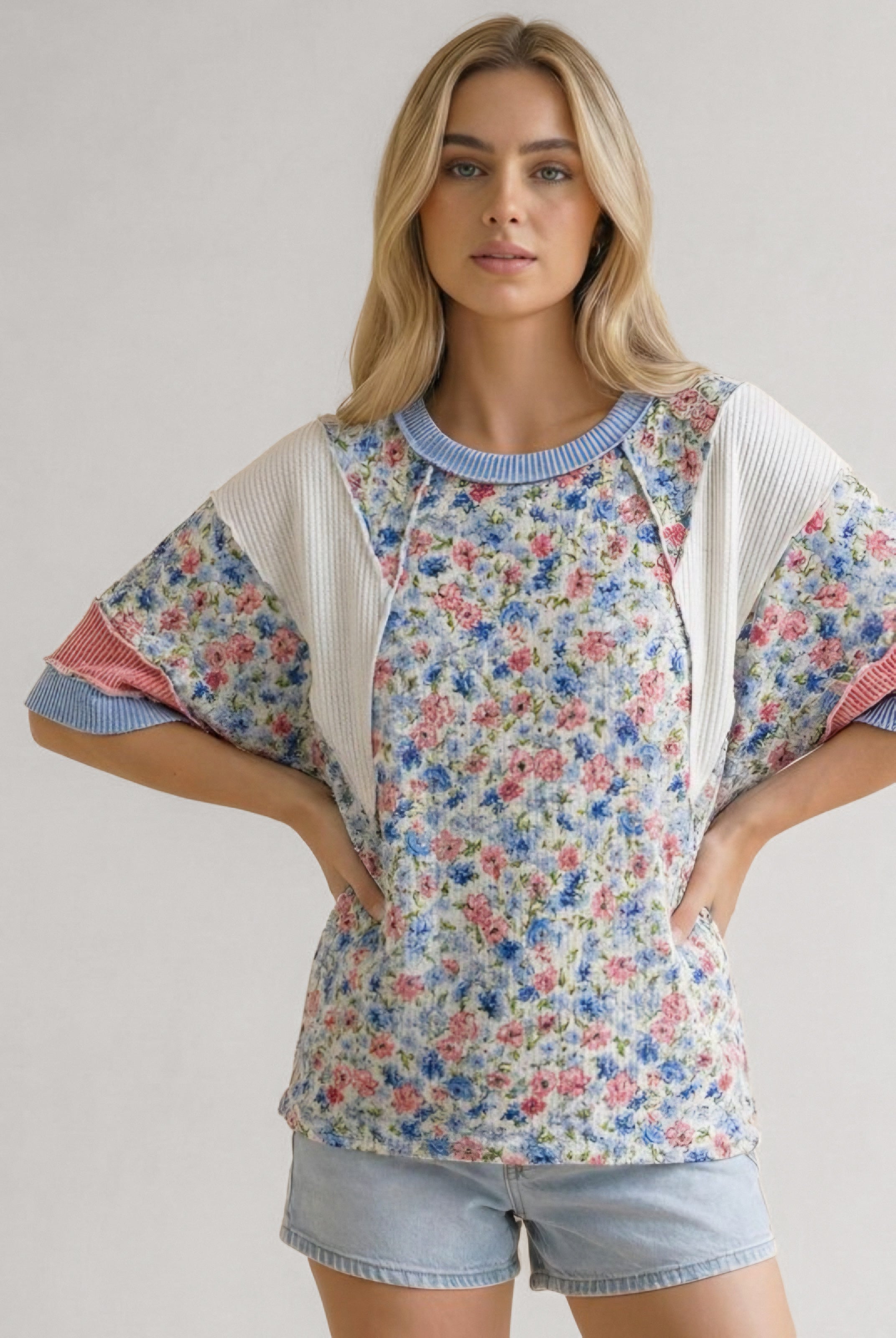 Woman wearing blue floral mixed media top with ribbed cream and coral sleeves paired with light denim shorts