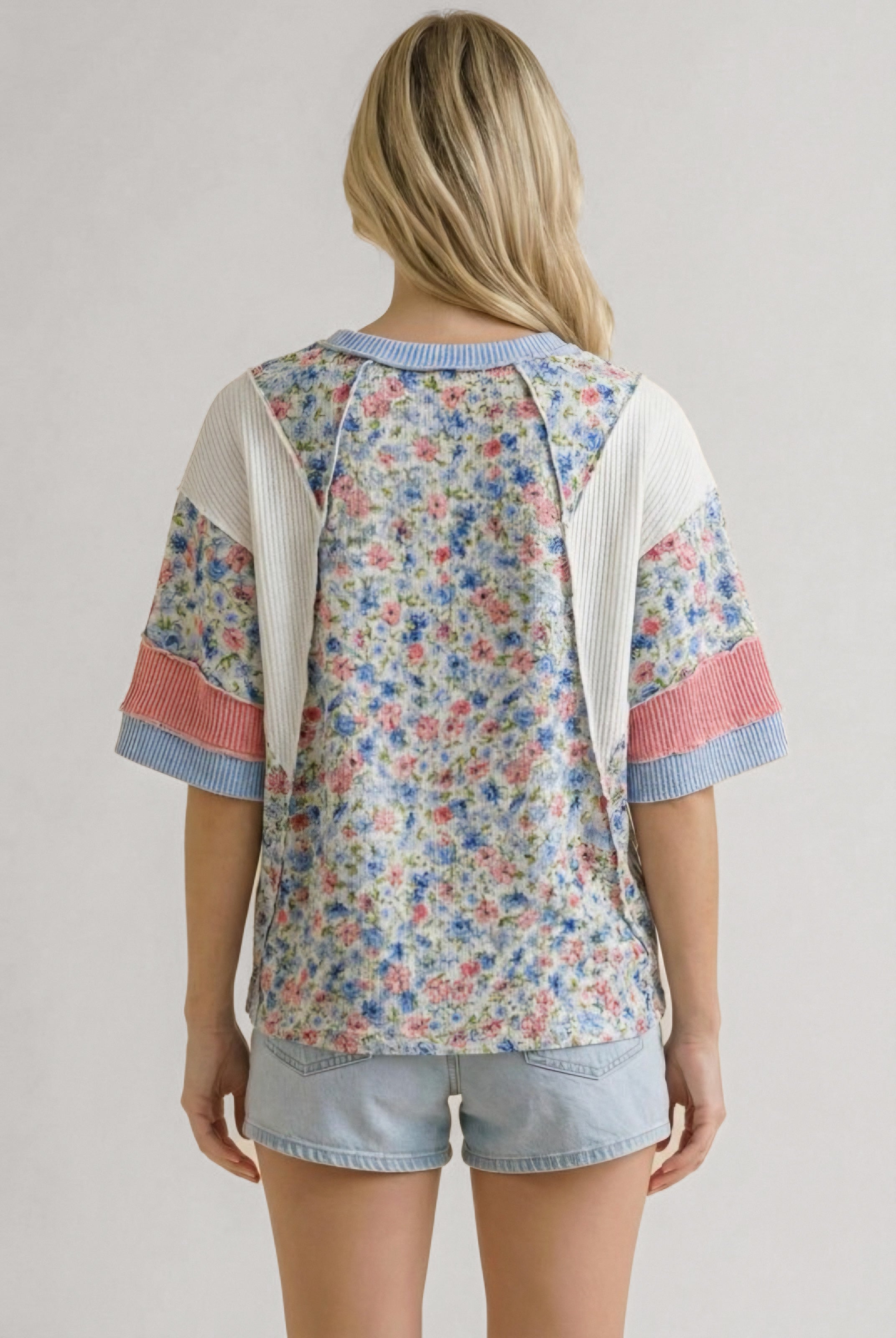 Back view of woman wearing mixed media floral top with blue and pink ribbed trim and light denim shorts