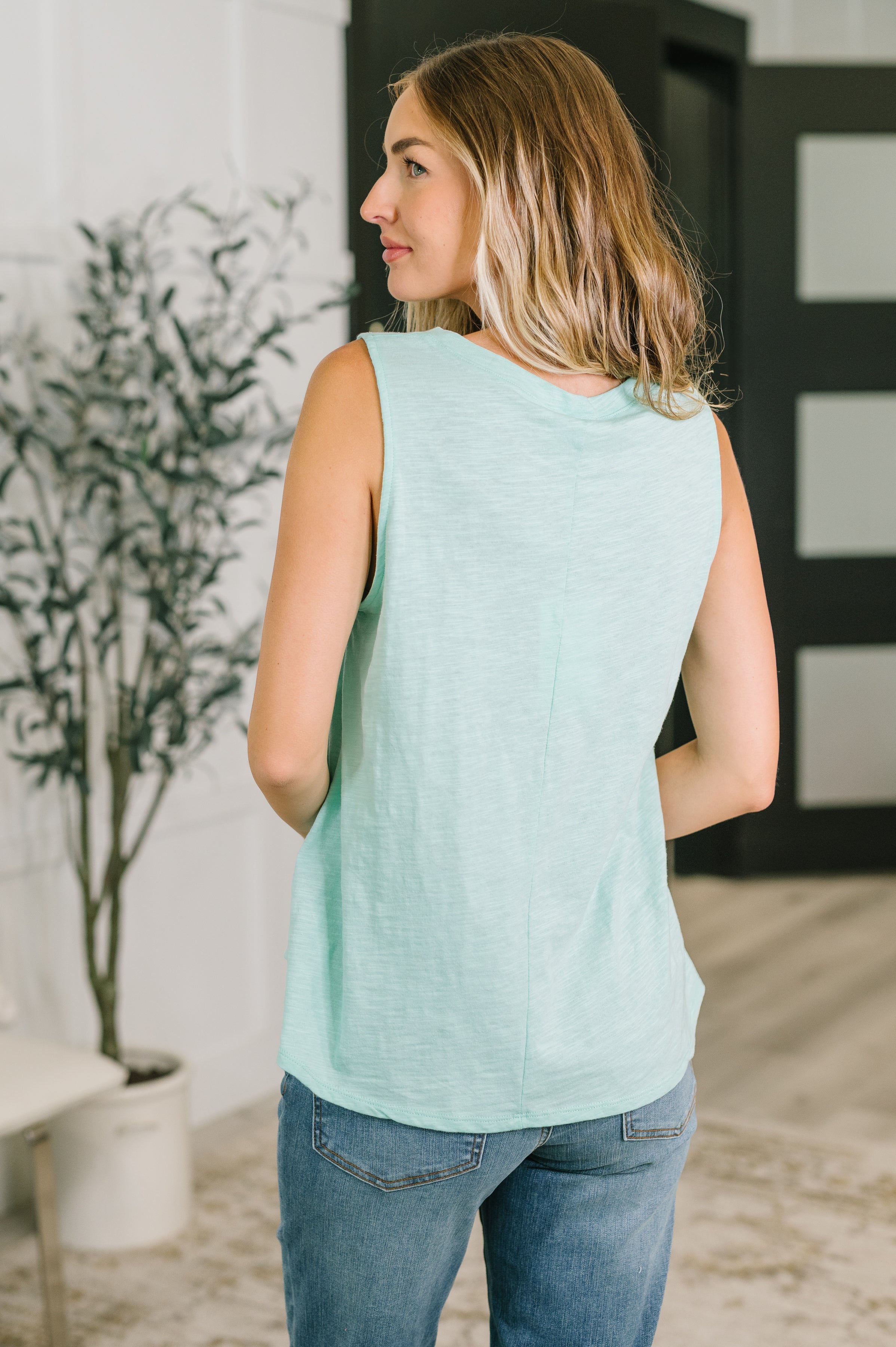 Woman in a soft mint sleeveless top with relaxed fit styled with casual jeans in a bright eclectic indoor space