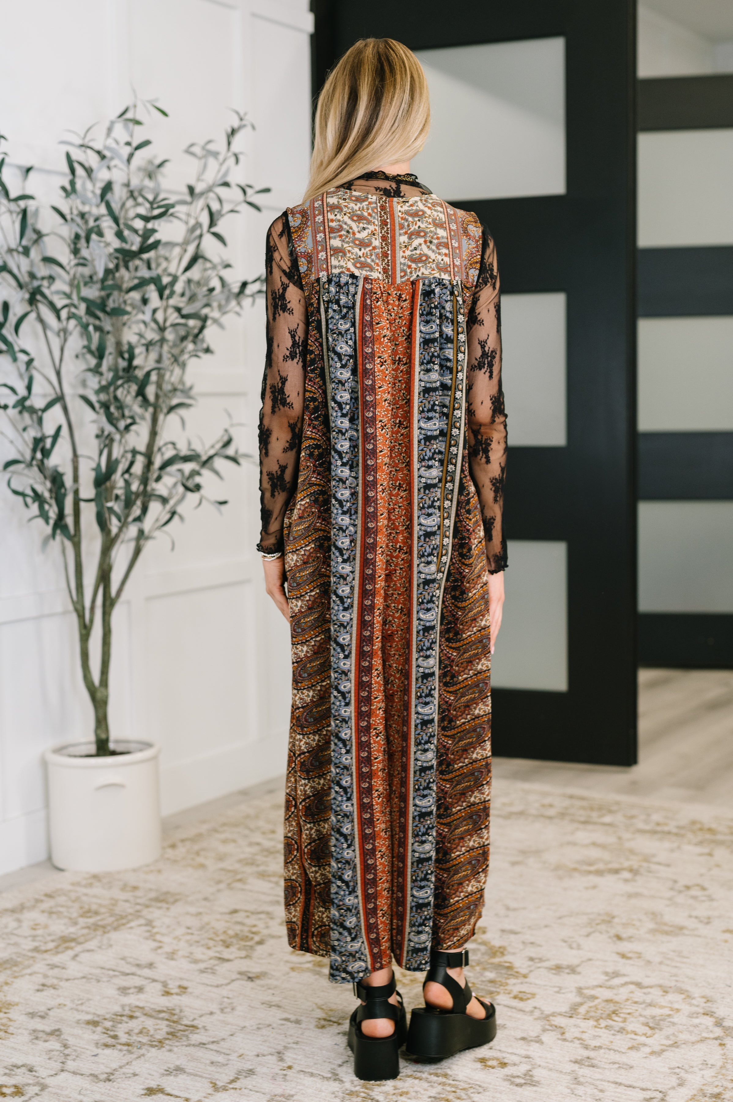 Woman wearing a brown mixed print jumpsuit with sheer black floral sleeves standing indoors