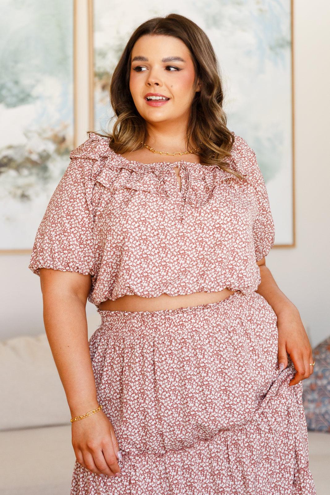 Plus size woman wearing a rose floral crop top with ruffle details and matching high-waisted skirt indoors