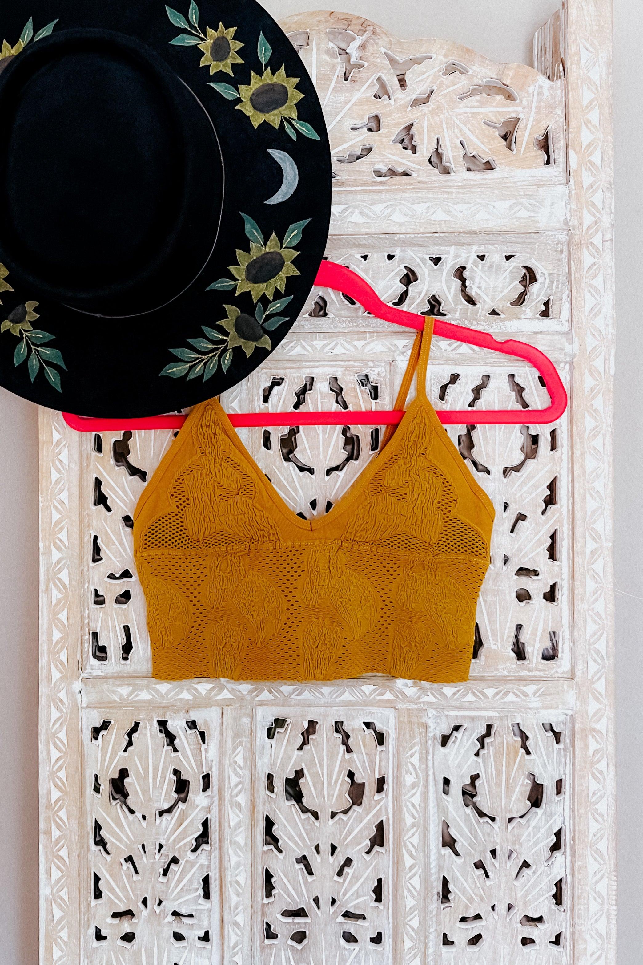 Mustard yellow seamless brami with textured floral pattern hanging on pink hanger against carved wooden screen with black hat nearby