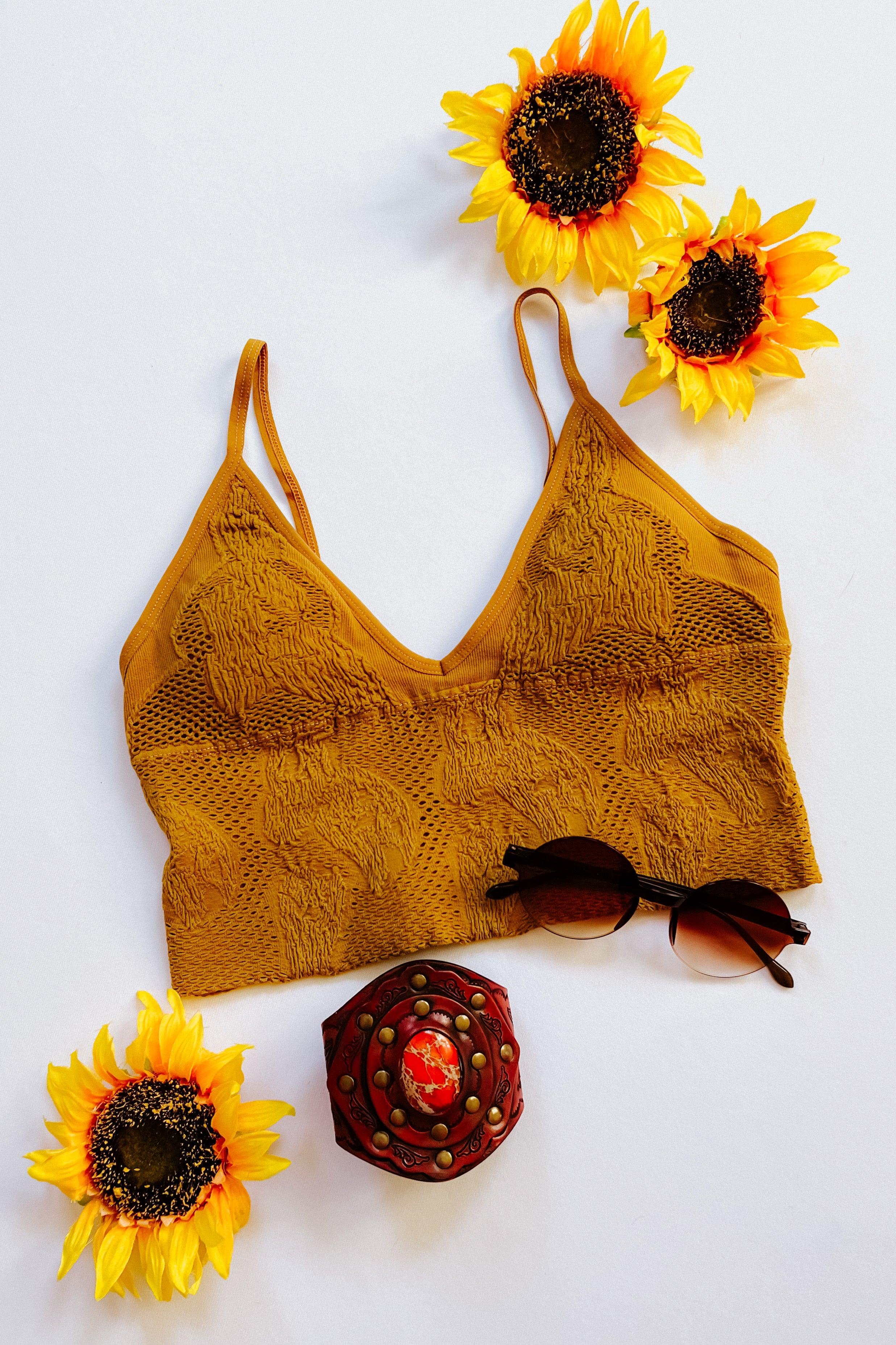 Mustard seamless padded brami with textured floral pattern styled flat with sunglasses, decorative box, and sunflowers on white surface