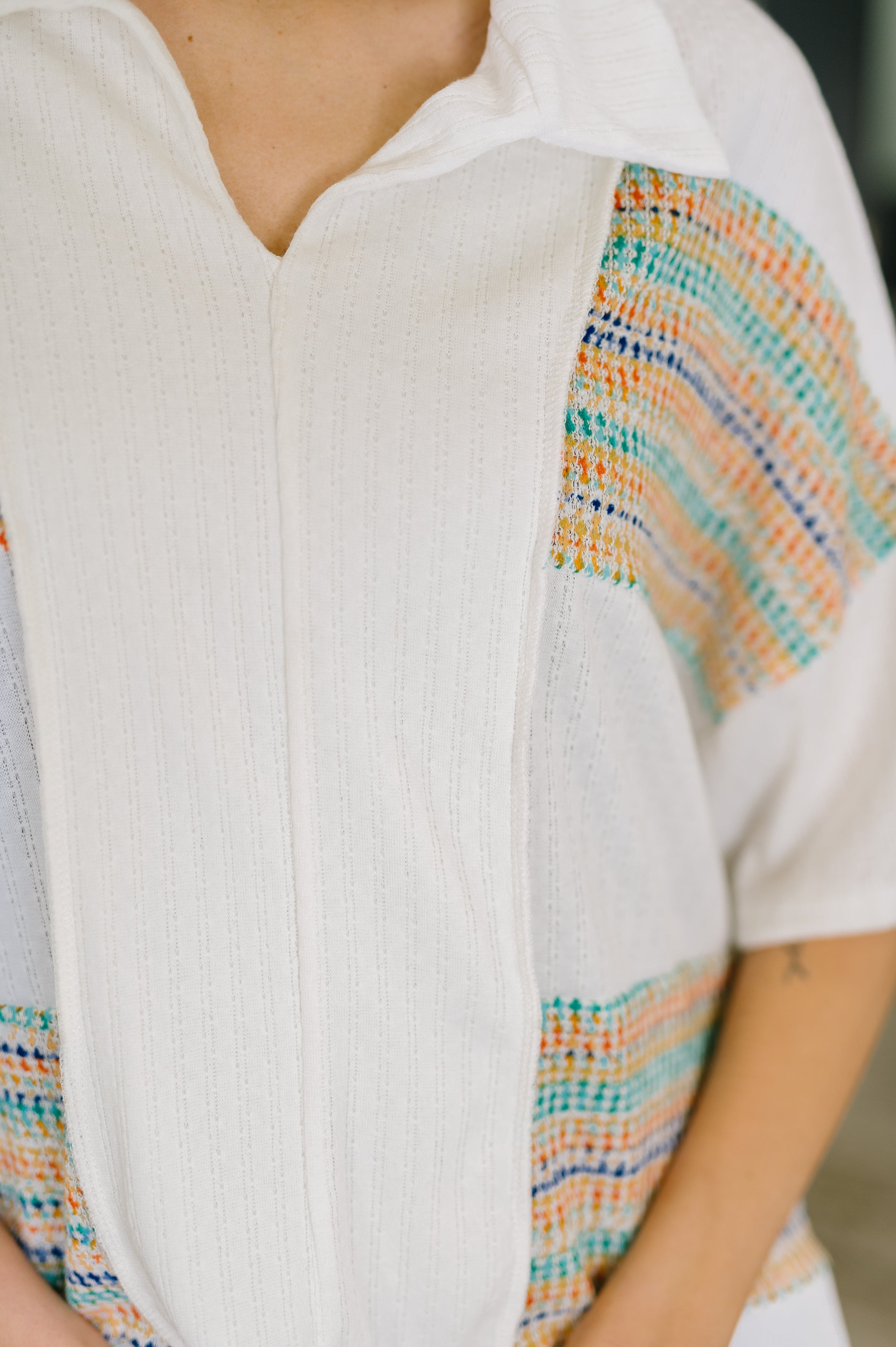 Close-up of person wearing cream knit top with collared v-neck and colorful textured stripes in an eclectic setting