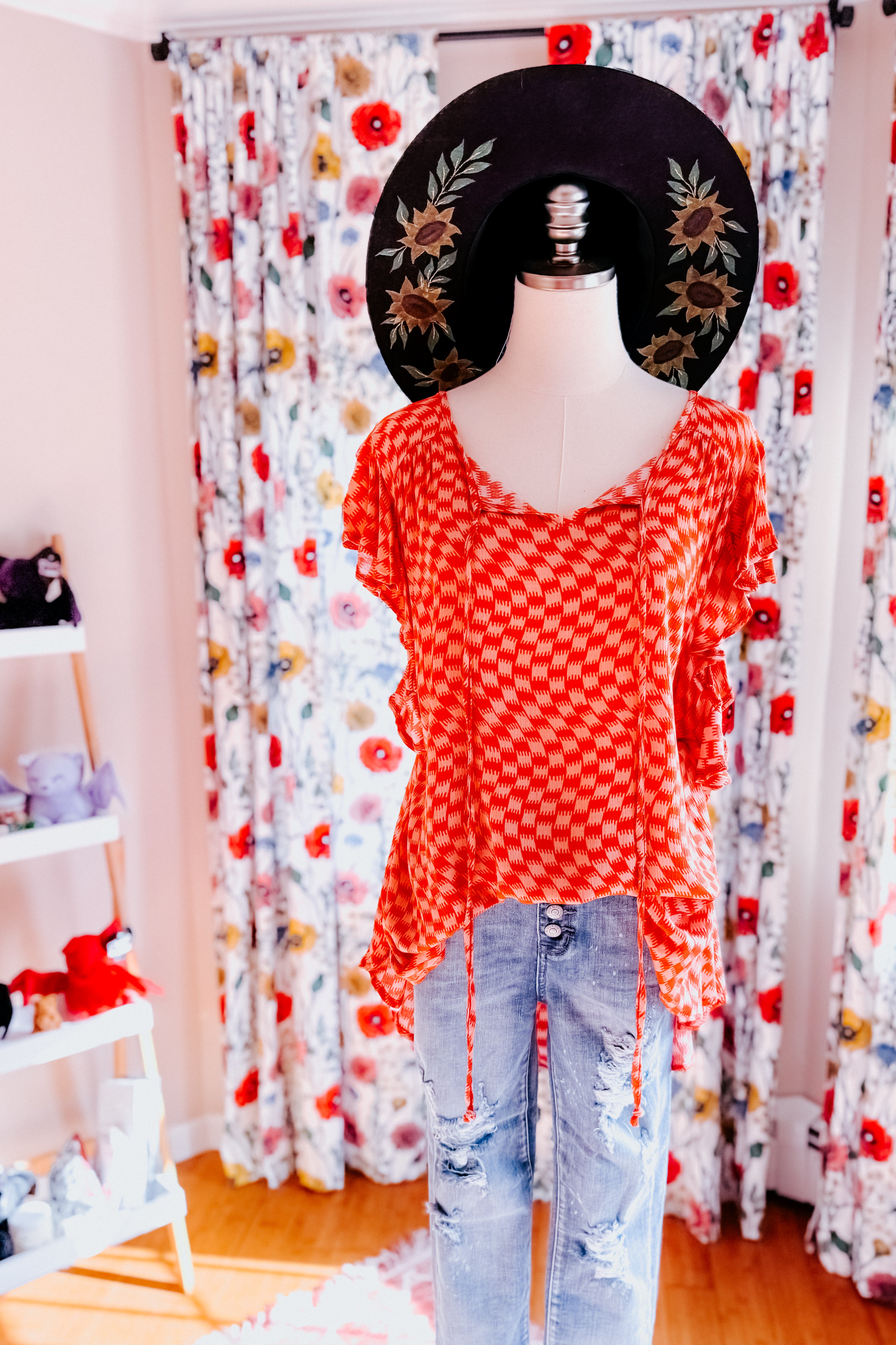 Mannequin wearing bright orange houndstooth butterfly sleeve top paired with distressed blue jeans and black wide-brimmed hat indoors