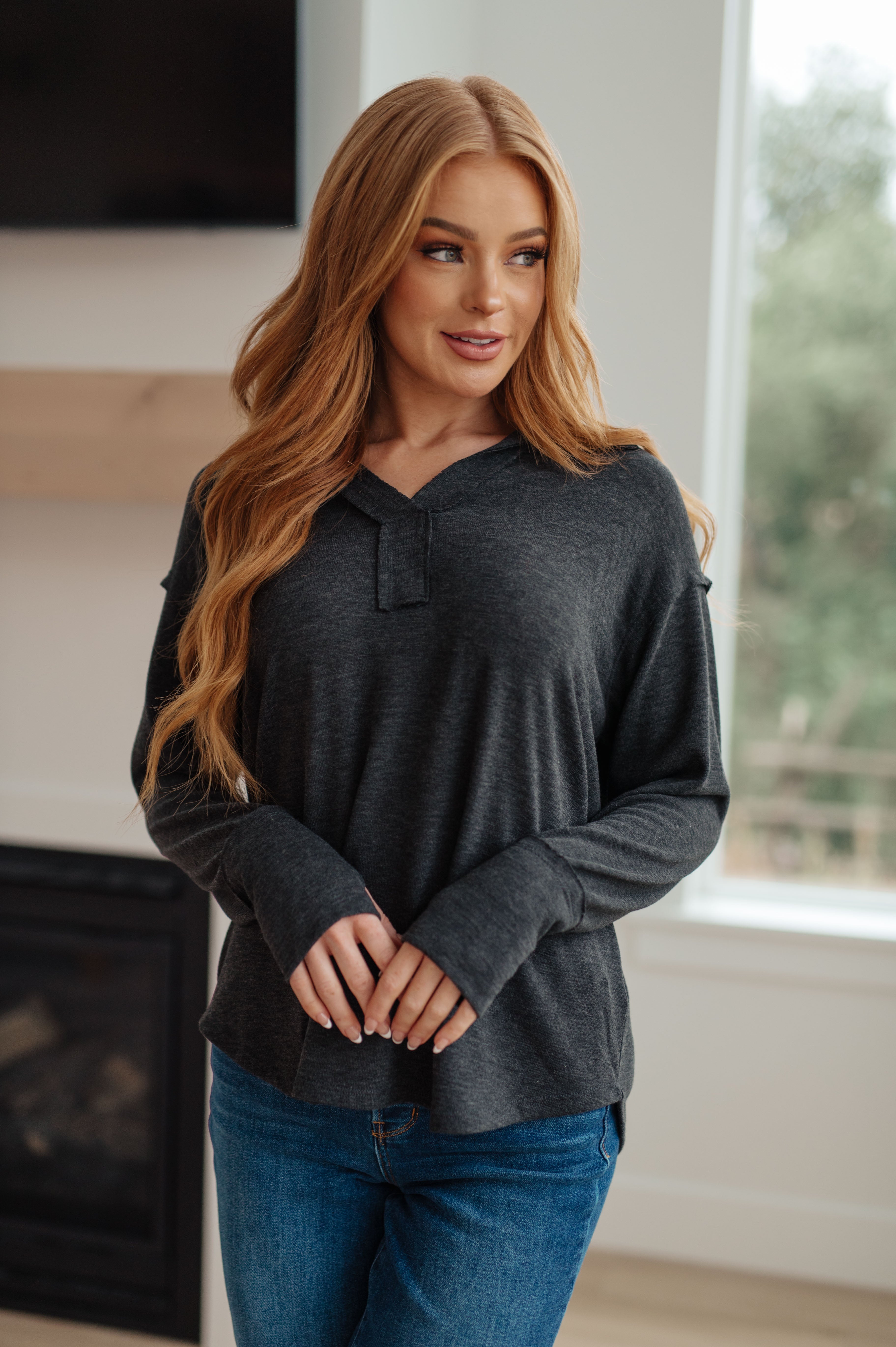 Blonde woman wearing charcoal long sleeve Good Luck Charm top with relaxed fit paired with blue jeans by bright window