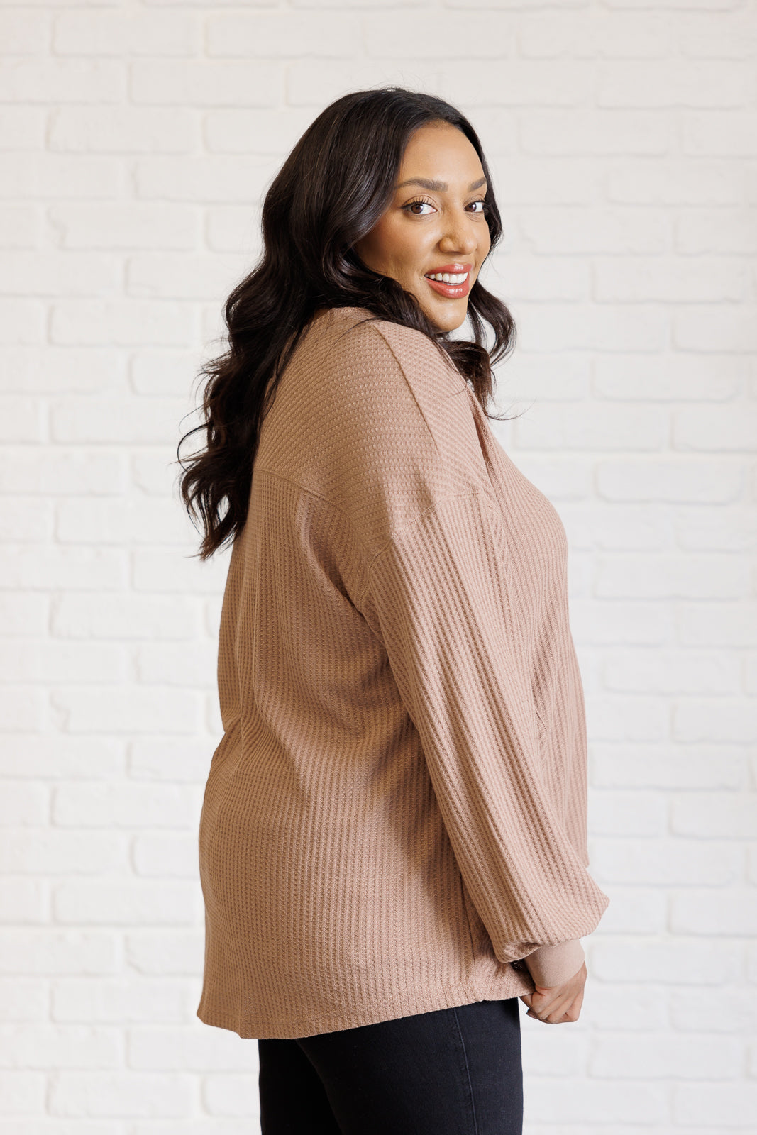 Smiling woman modeling a coffee textured V neck top with long sleeves and a scooped hem indoors