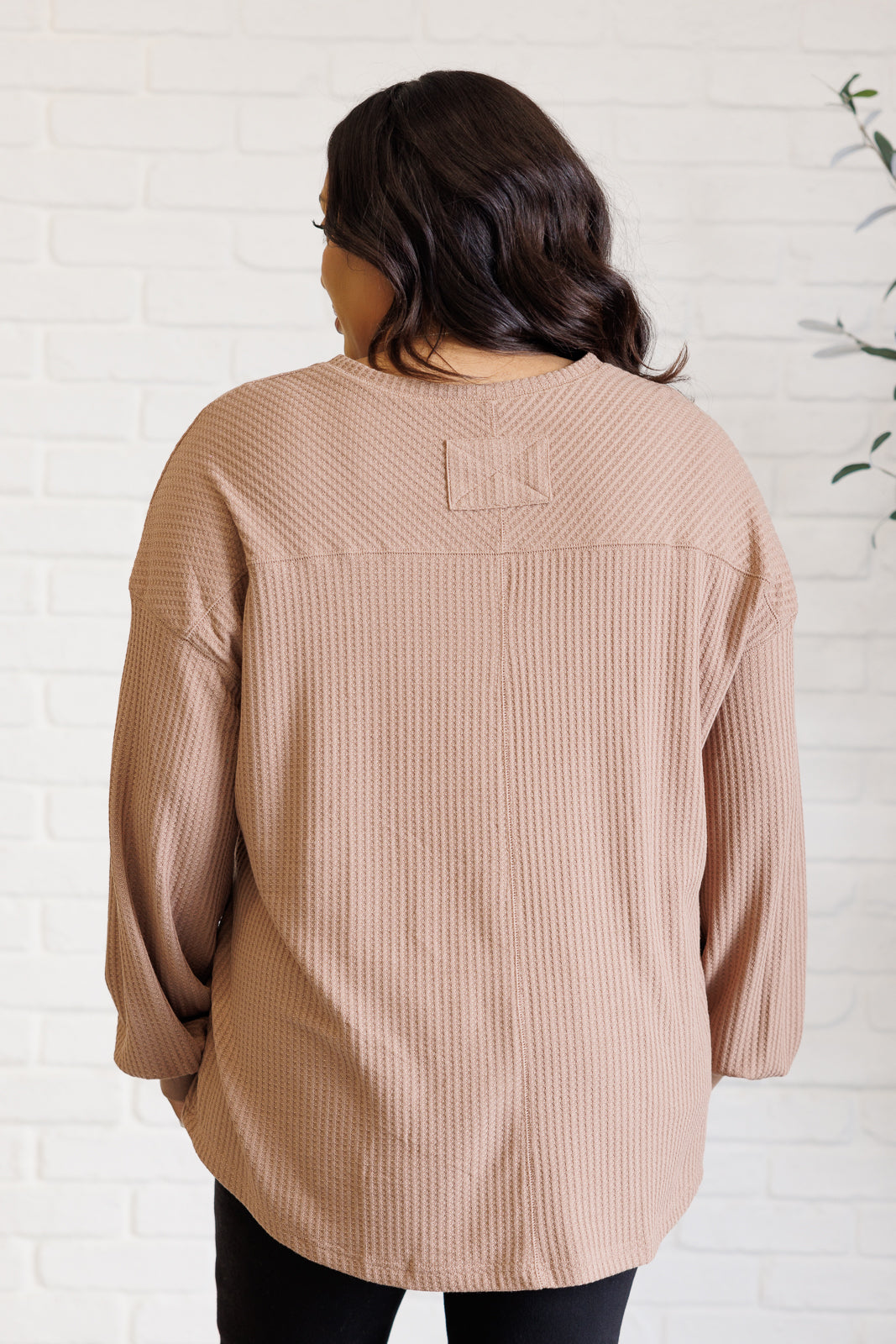 Back view of woman wearing a coffee textured top with drop shoulders and curved hem indoors
