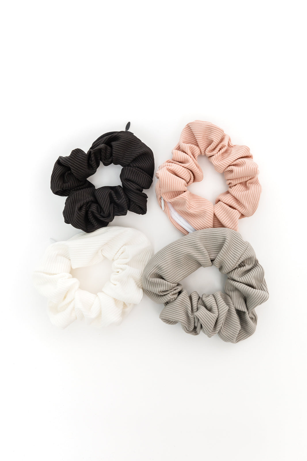 Set of four ribbed scrunchies in black, pink, white, and gray tones with hidden zipper pockets as stylish accessories.