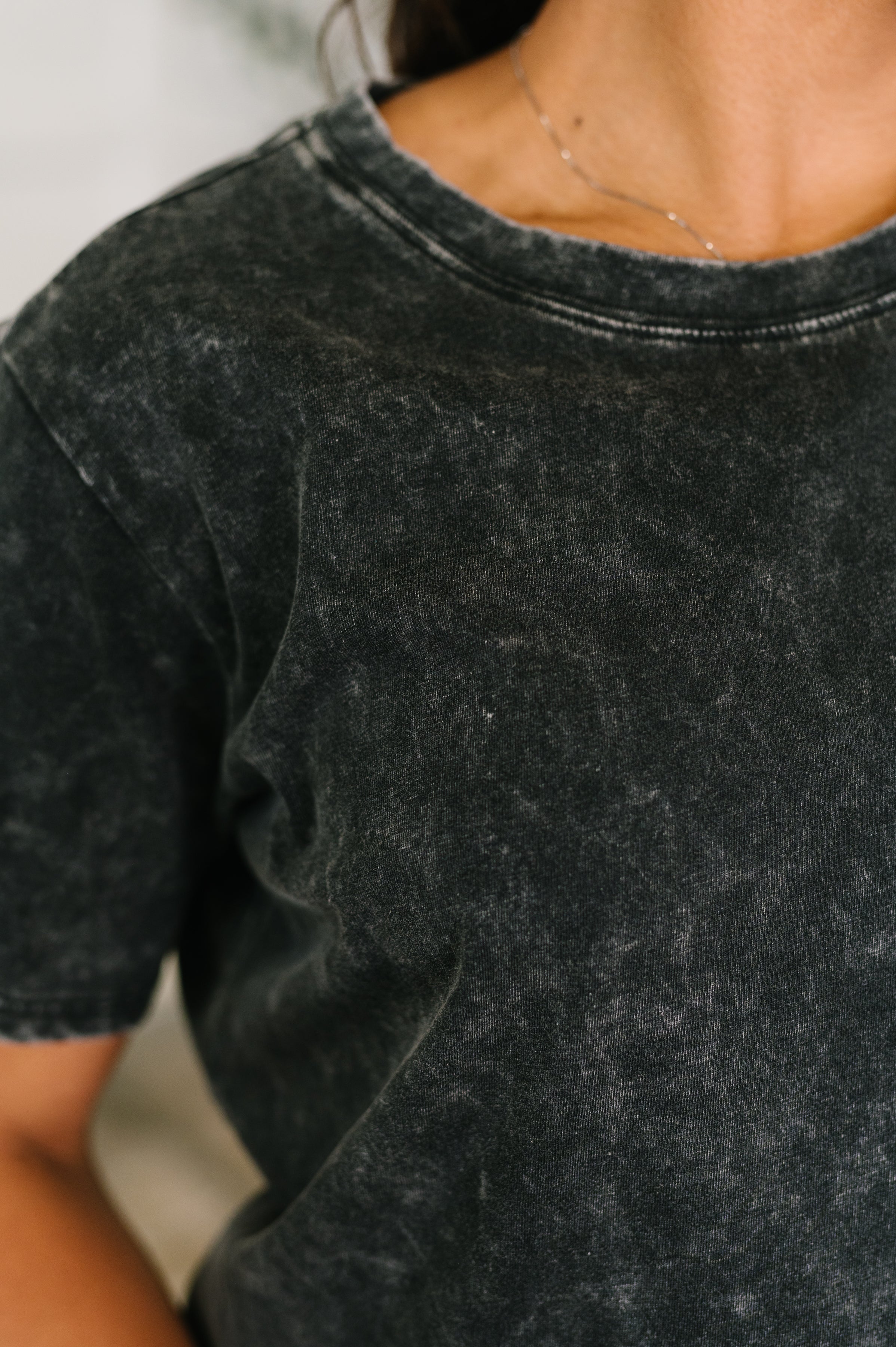 Close-up of soft mineral wash ash black tee with relaxed fit and crew neckline, styled with delicate silver necklace
