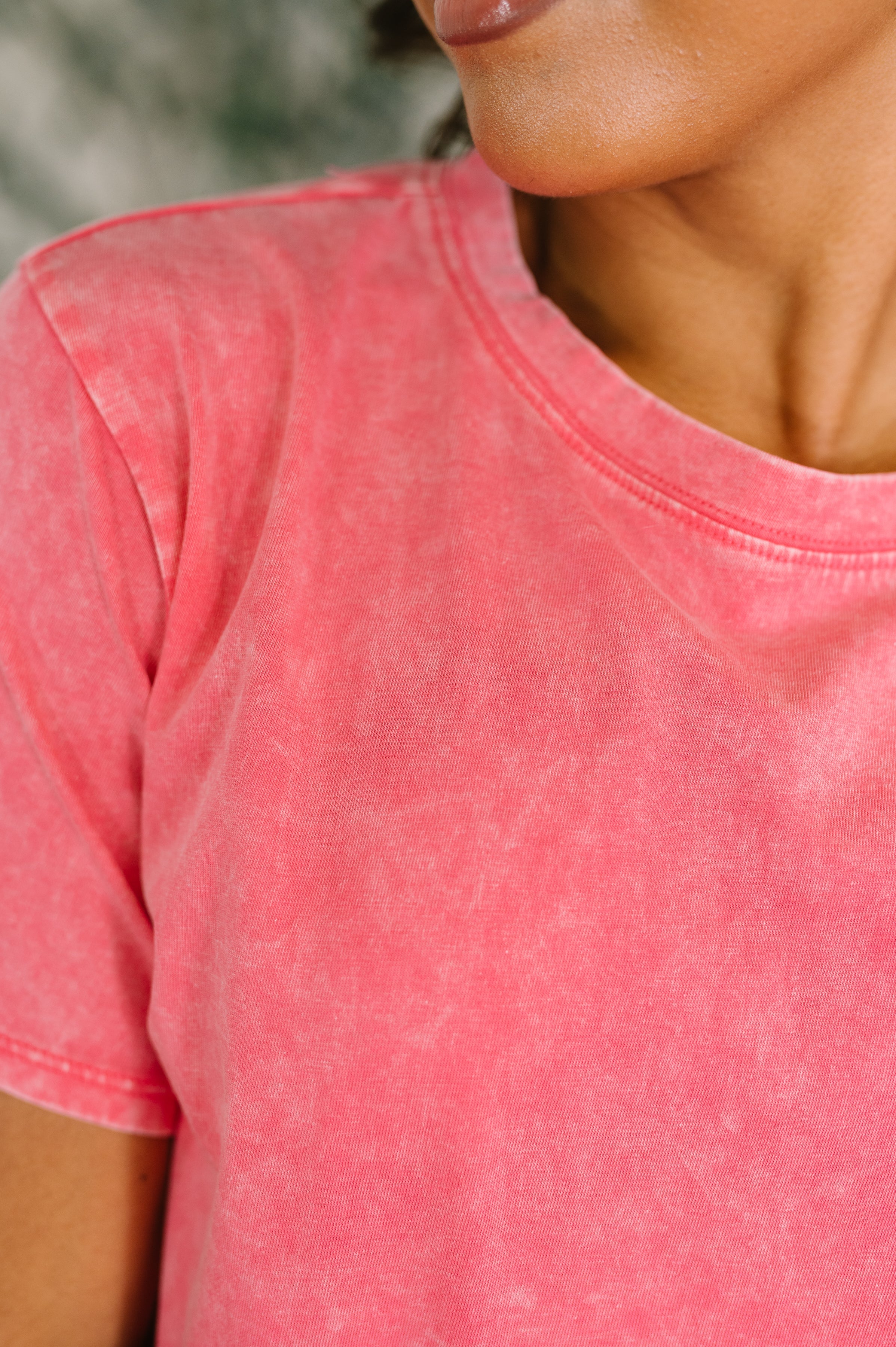Close-up of fuchsia mineral wash tee with crew neck and short sleeves on person with medium skin tone and natural lip color