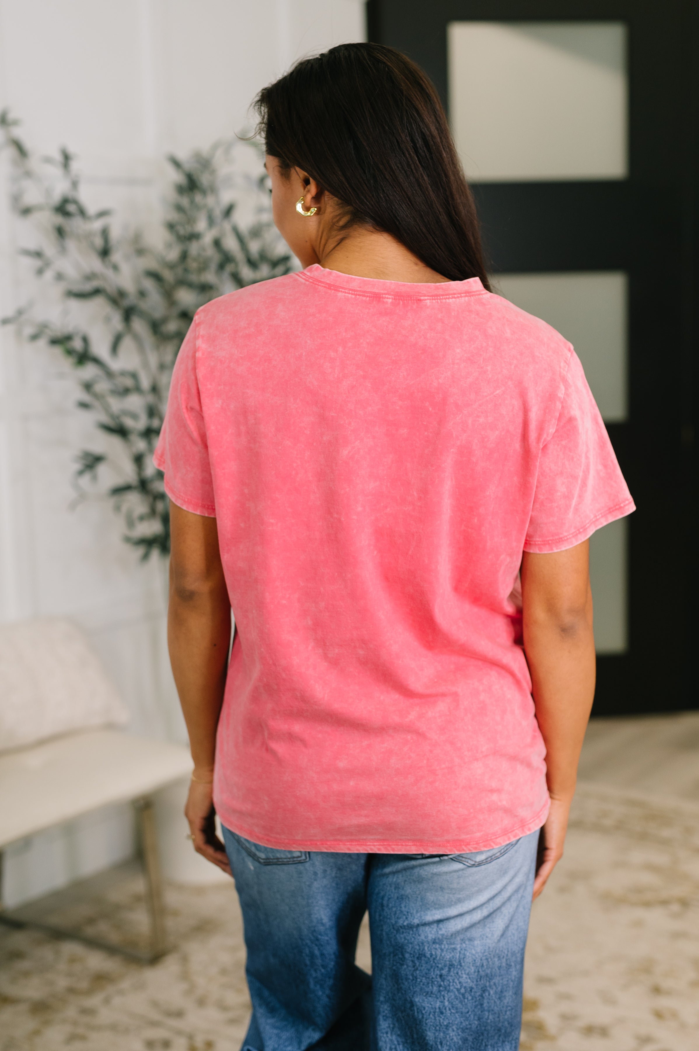 Back view of woman wearing a fuchsia mineral wash tee with relaxed fit paired with medium wash jeans indoors