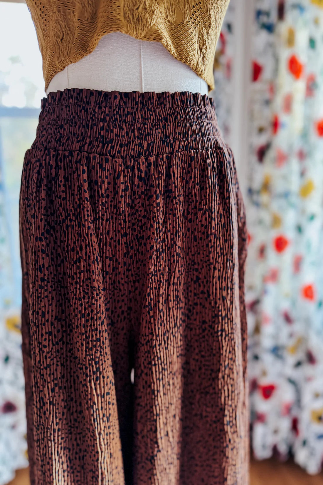 Brown high rise wide leg pants with textured abstract print displayed on mannequin wearing mustard top in cozy room setting