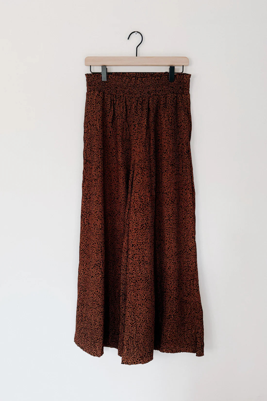 Brown Harmony high rise wide leg pants with subtle textured pattern hanging on wooden hanger against plain wall