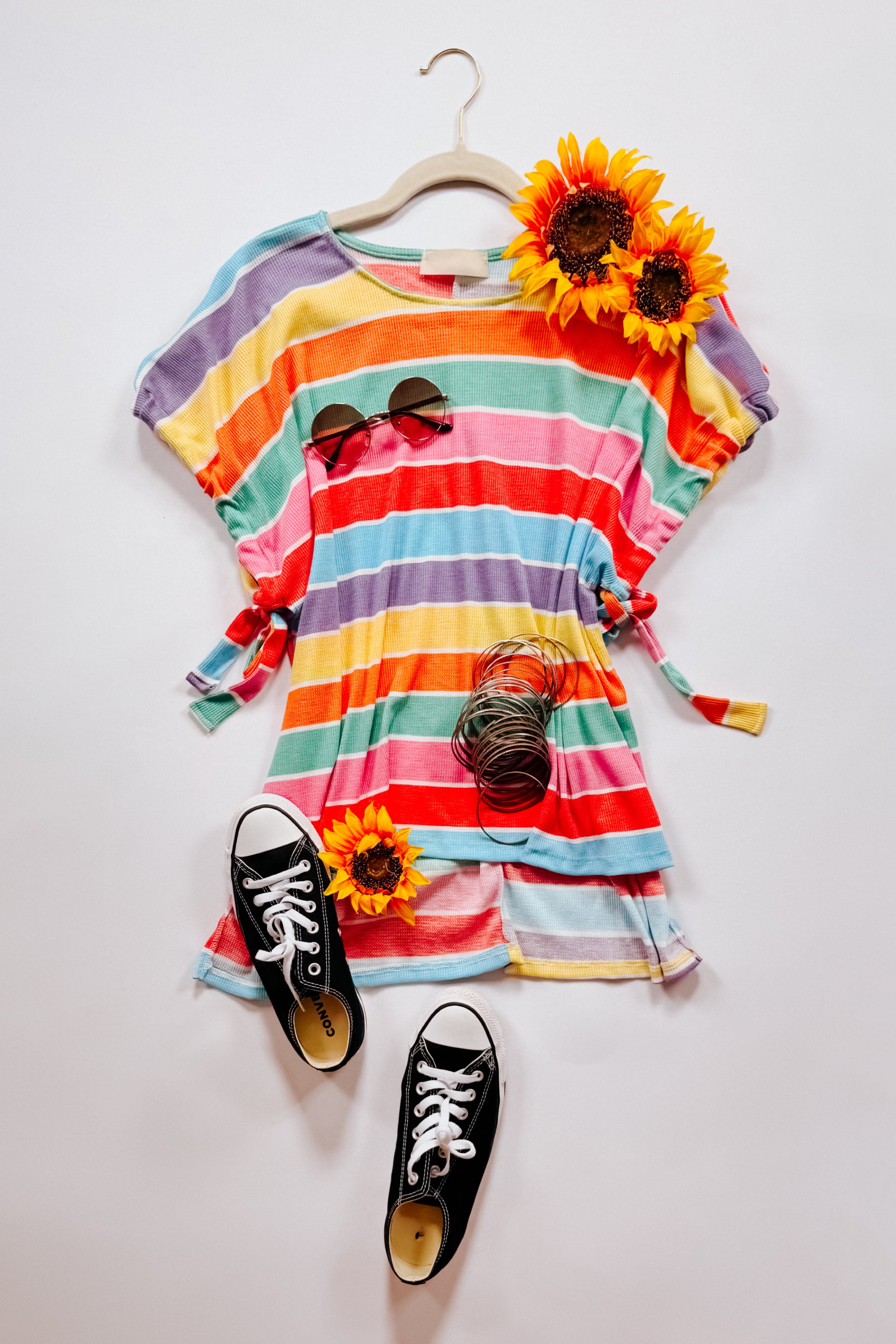 Multicolor striped dolman sleeve top with side ties styled with sunglasses, bracelets, black sneakers, and sunflowers on white background