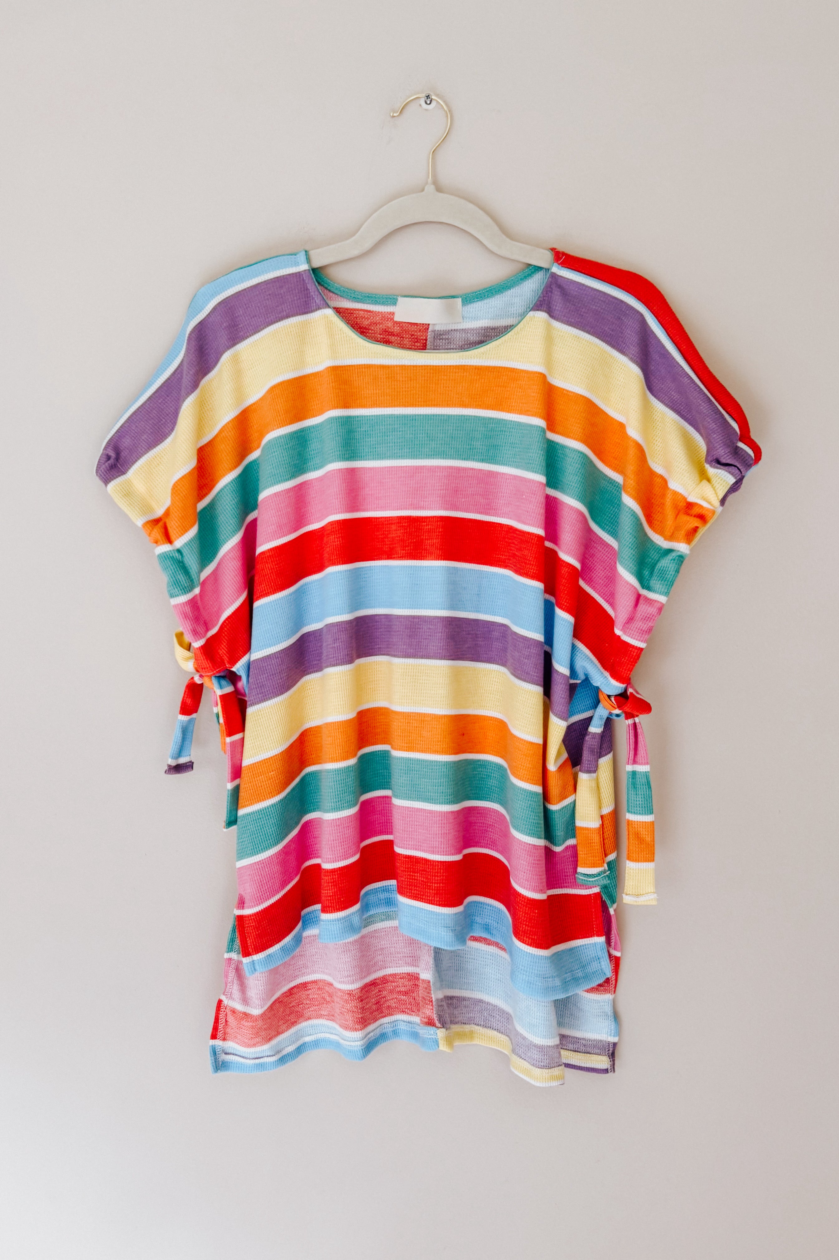 Multicolor striped dolman sleeve top with side ties hanging on a beige hanger against a neutral background