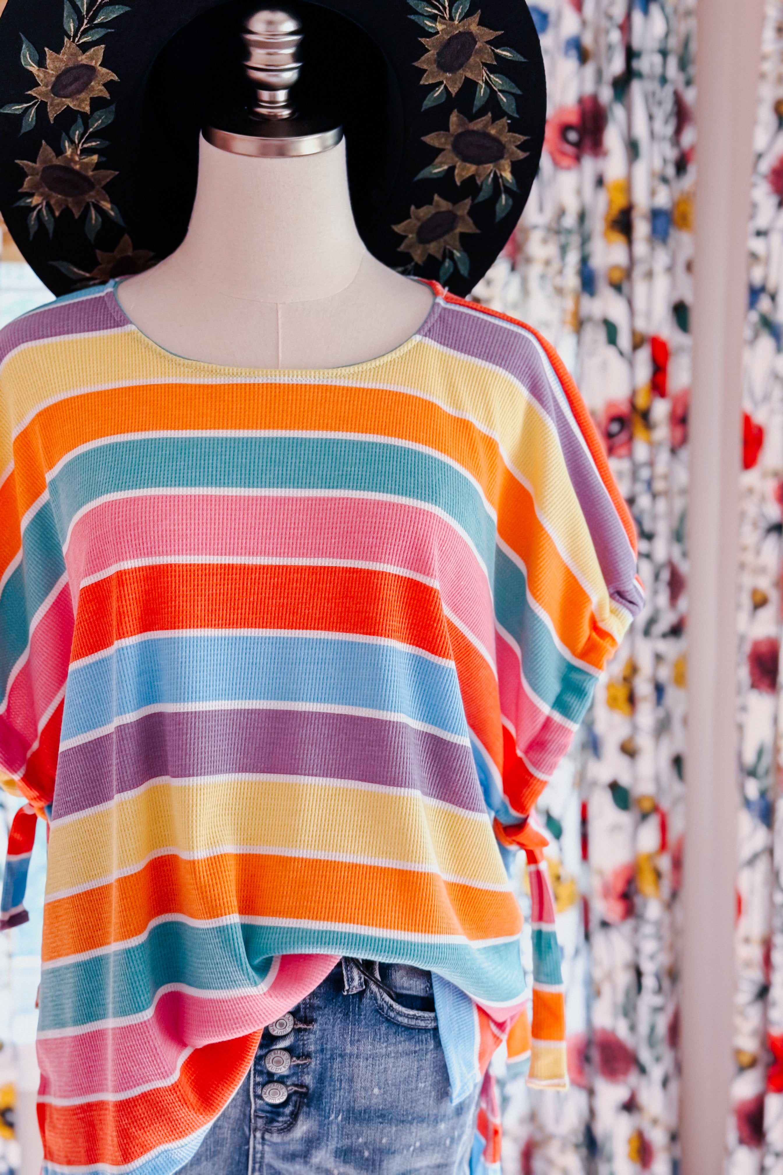 Multicolor striped dolman sleeve top with side ties styled on mannequin with denim shorts and embroidered black hat