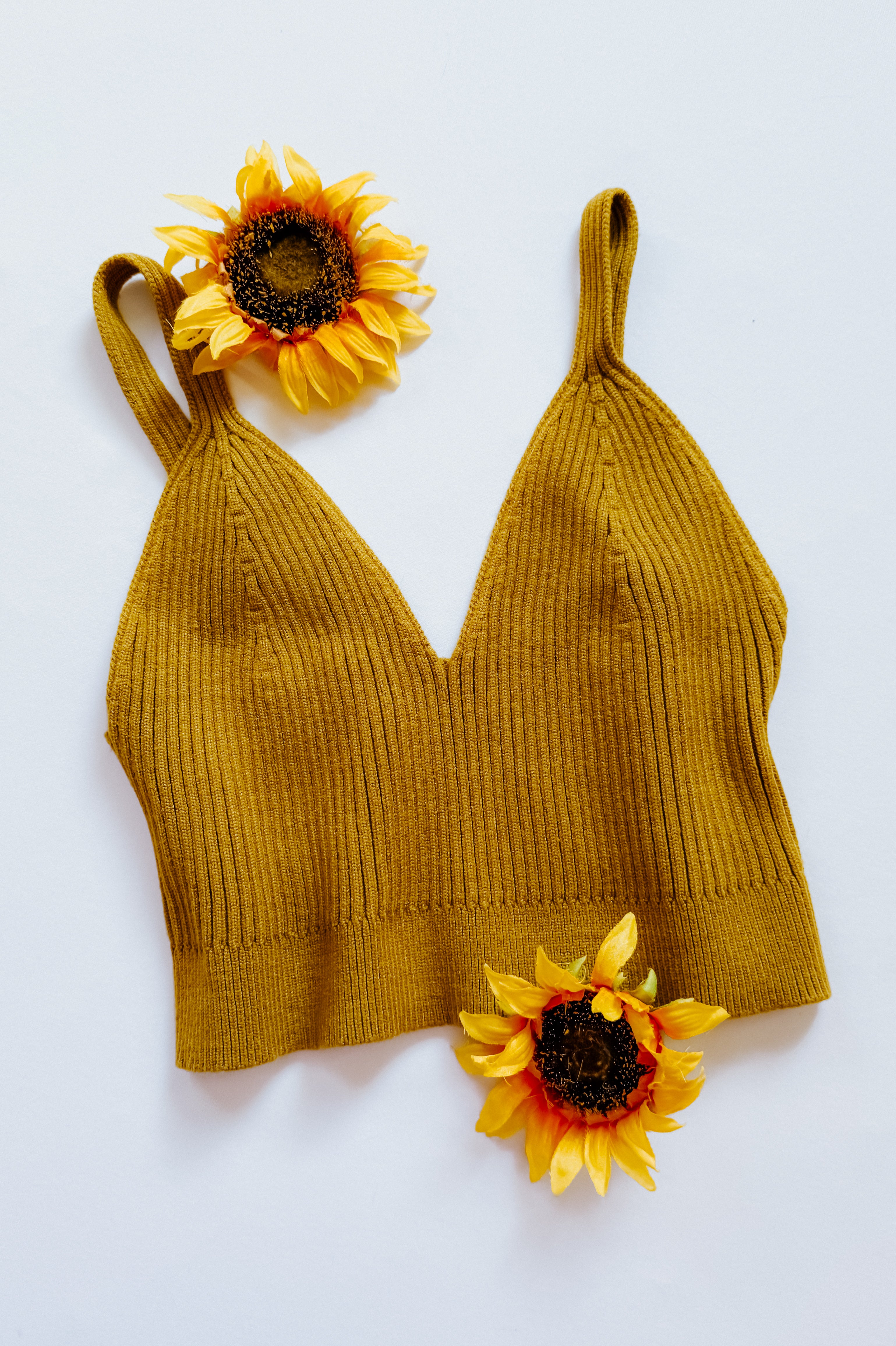 Mustard-colored rib knit brami bralette with narrow straps and deep V neckline displayed flat with two sunflowers on white background