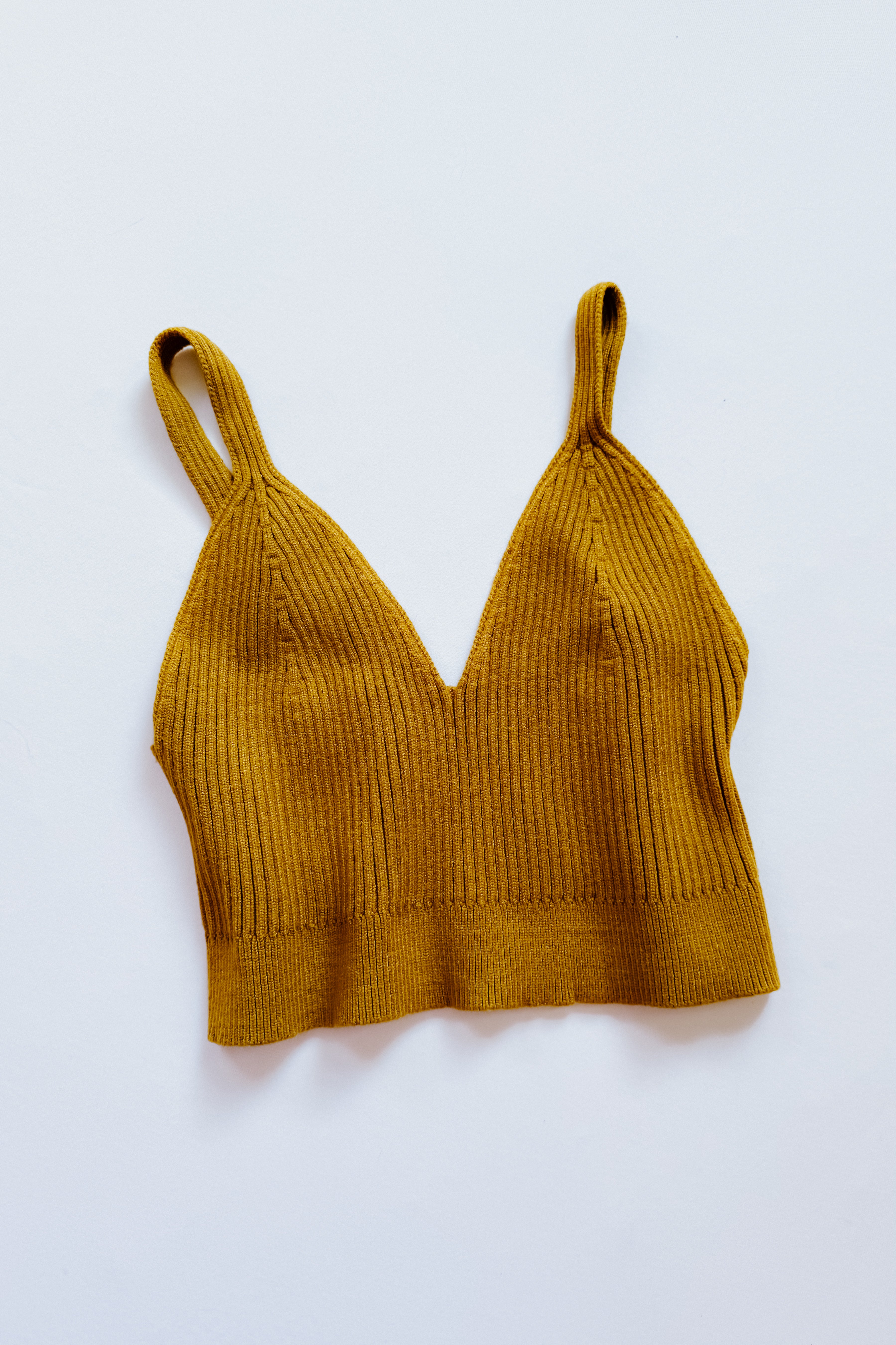 Mustard rib knit bralette with narrow straps and deep V neckline laid flat on a white surface
