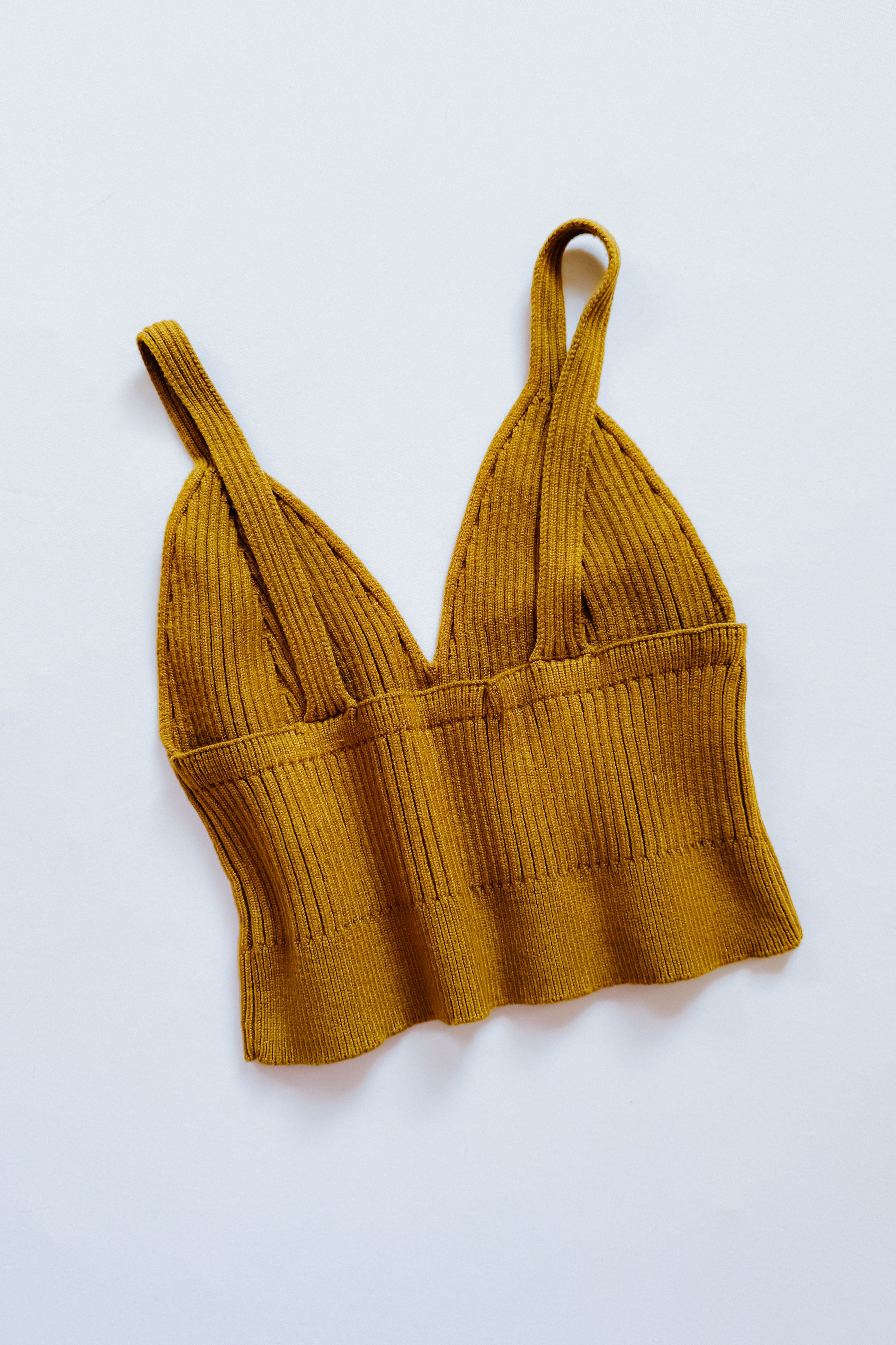 Mustard-colored rib knit brami bralette with wide straps and a deep V neckline laid flat on white background