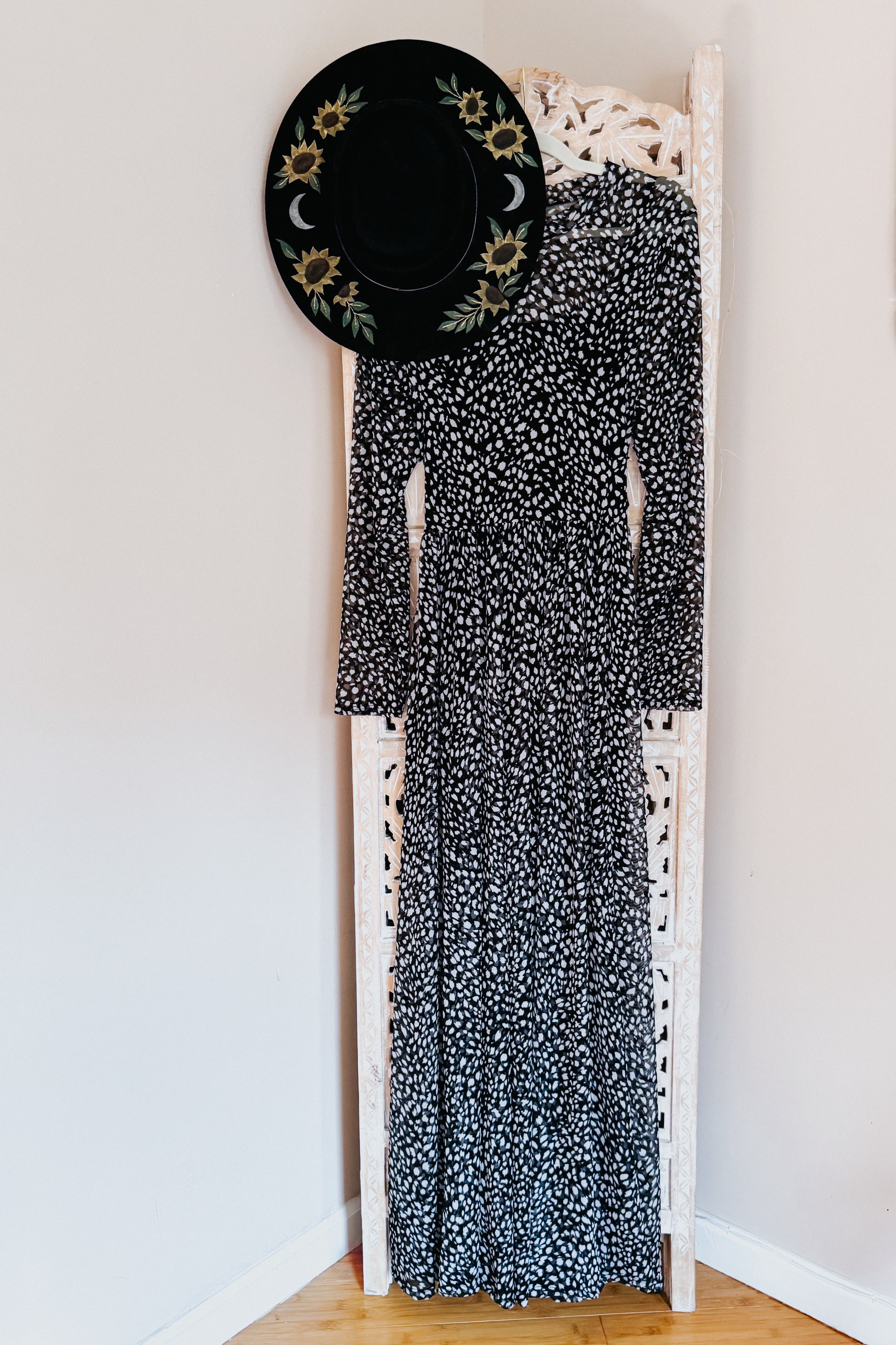 Black Hendrix long sleeve animal print mesh maxi dress hanging on carved white screen with black floral hat above