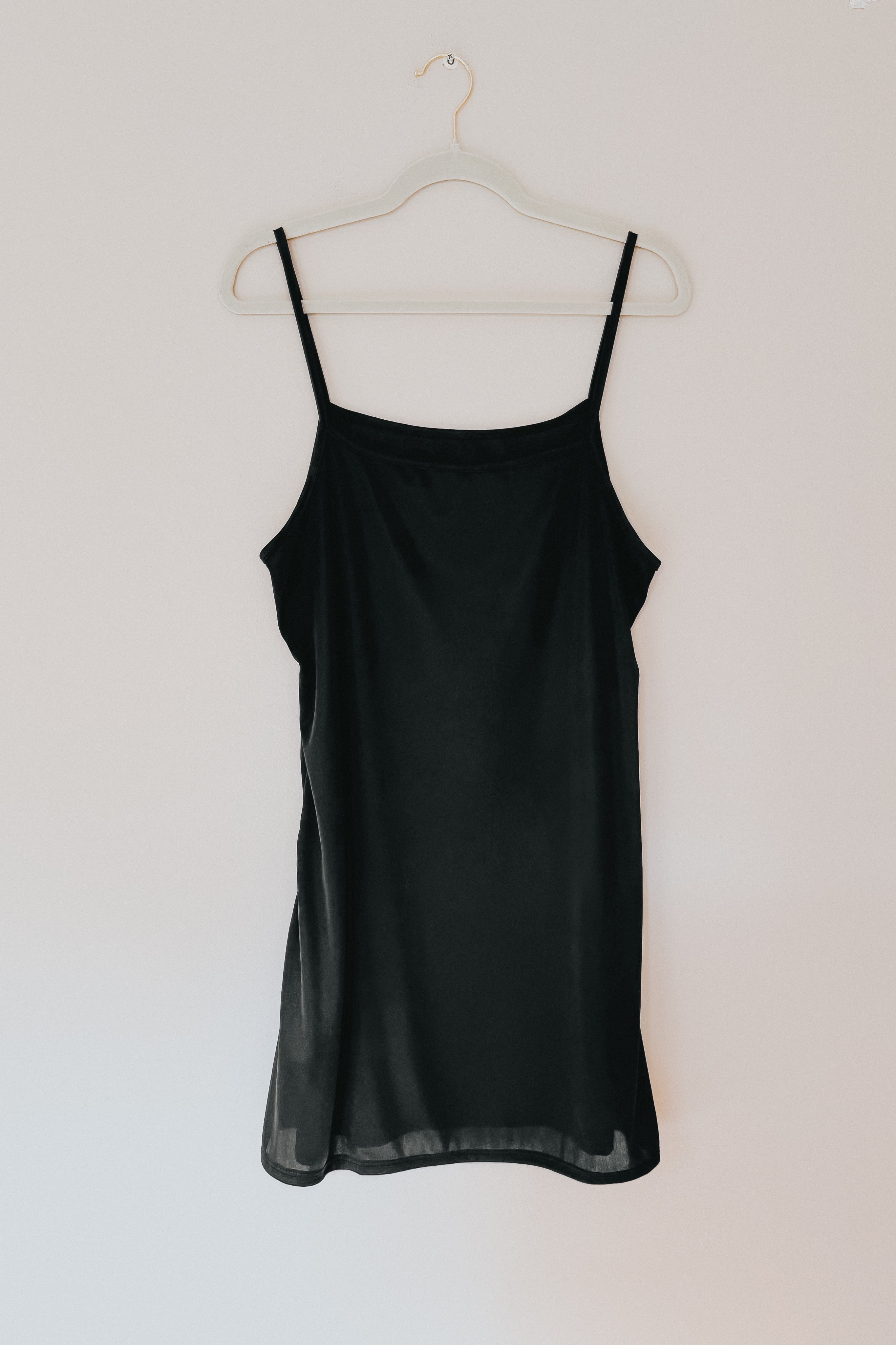 Black Hendrix sleeveless slip dress with thin straps hanging on beige wall background