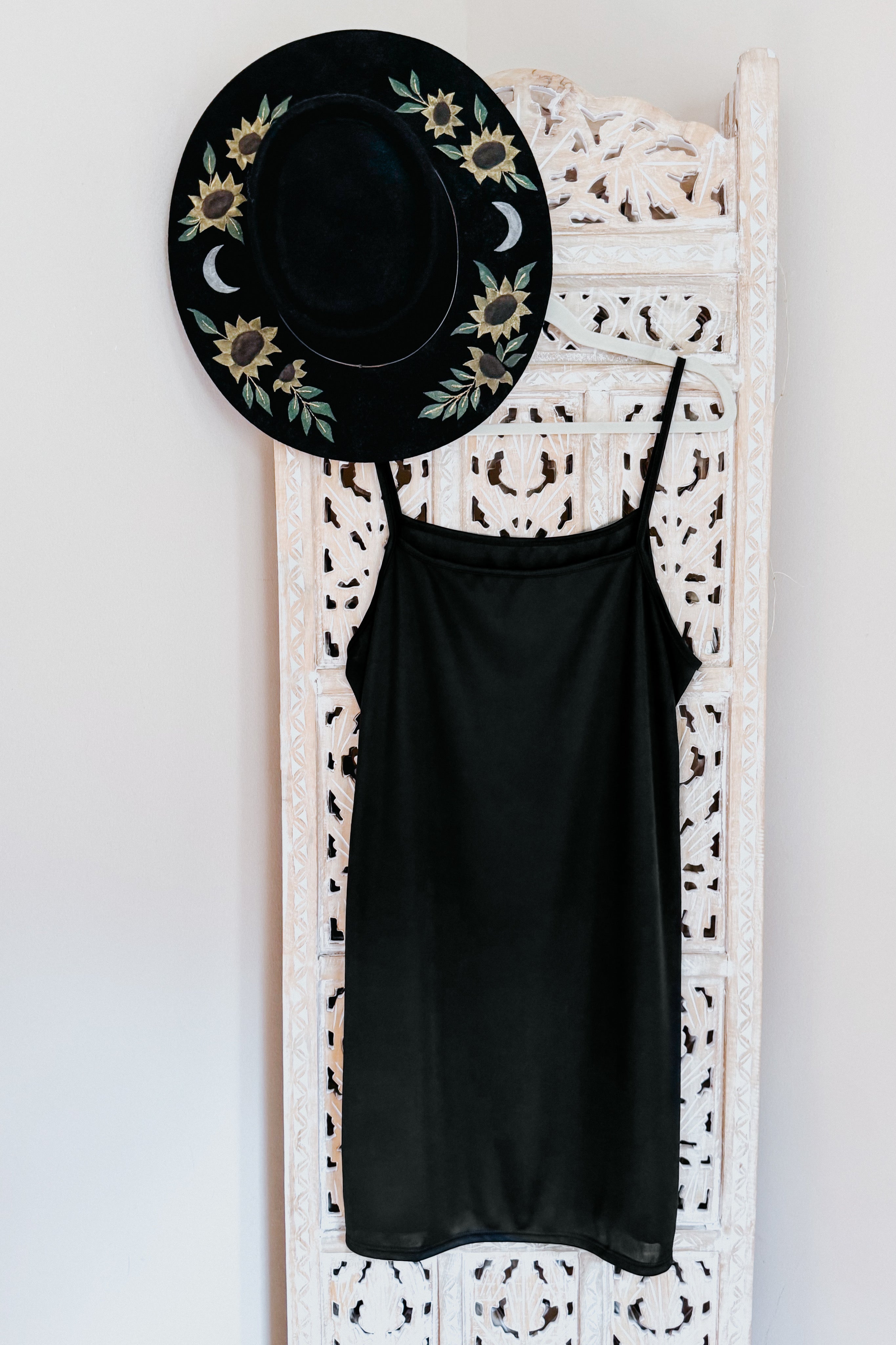 Black Hendrix sleeveless mesh midi slip dress hanging on carved white wooden panel with black floral painted hat above